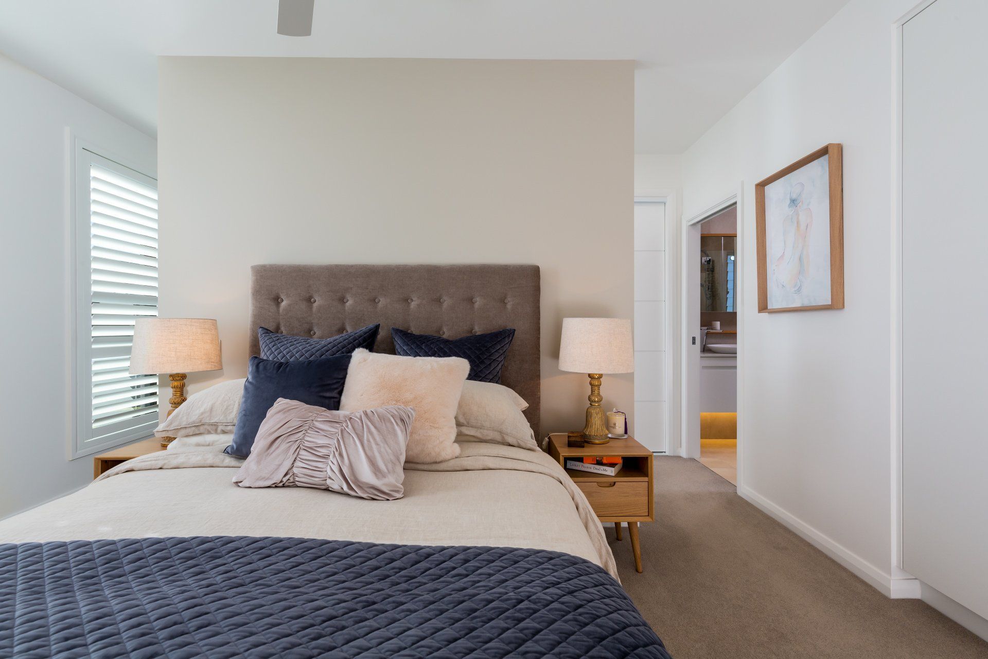 Bedroom with a beige upholstered headboard, two nightstands, and a doorway to a bathroom.