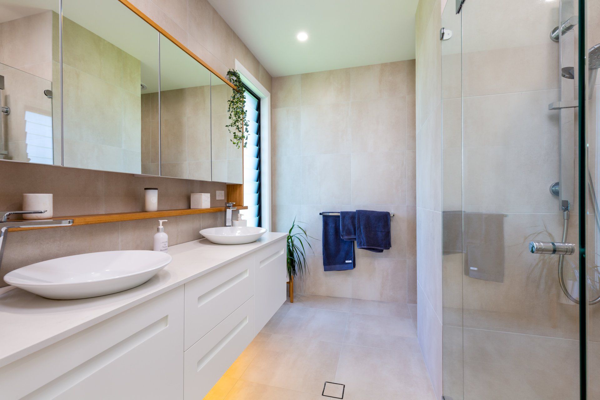 Modern bathroom with white vanity, vessel sinks, large mirror, glass shower, blue towels.