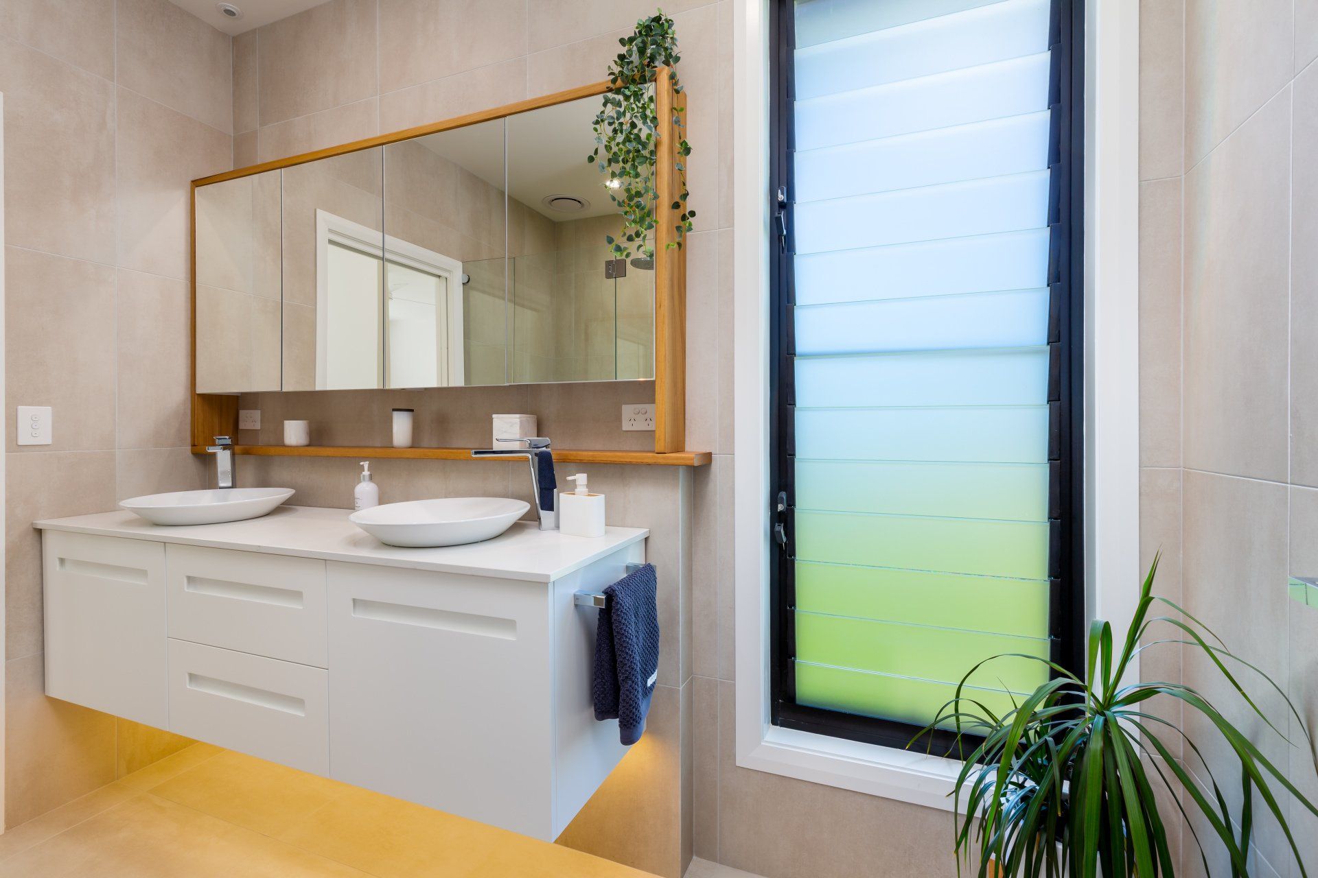 Modern bathroom with floating vanity, double sinks, large mirror, and louvered window.