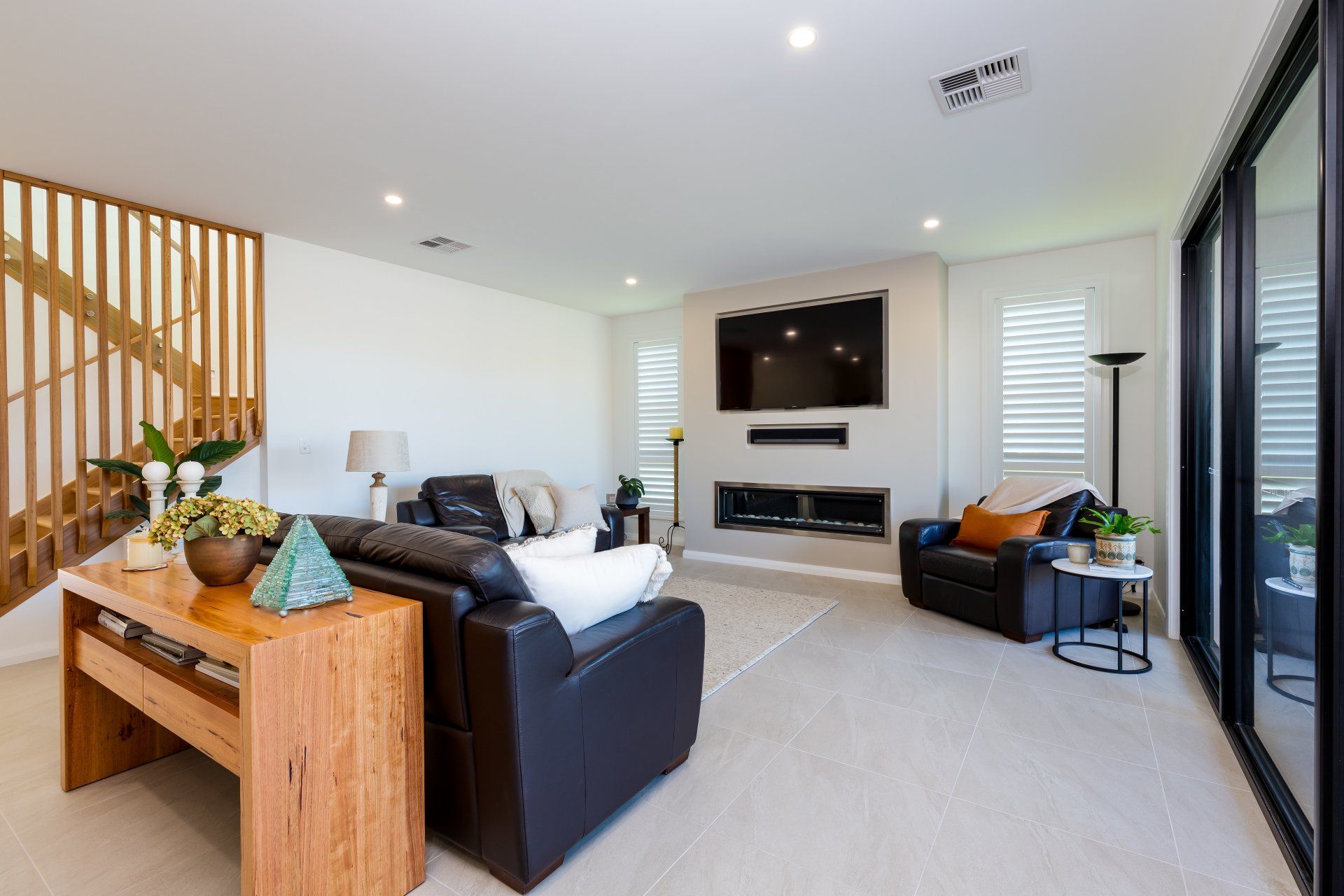 Modern living room with black leather couches, fireplace, and sliding glass doors.