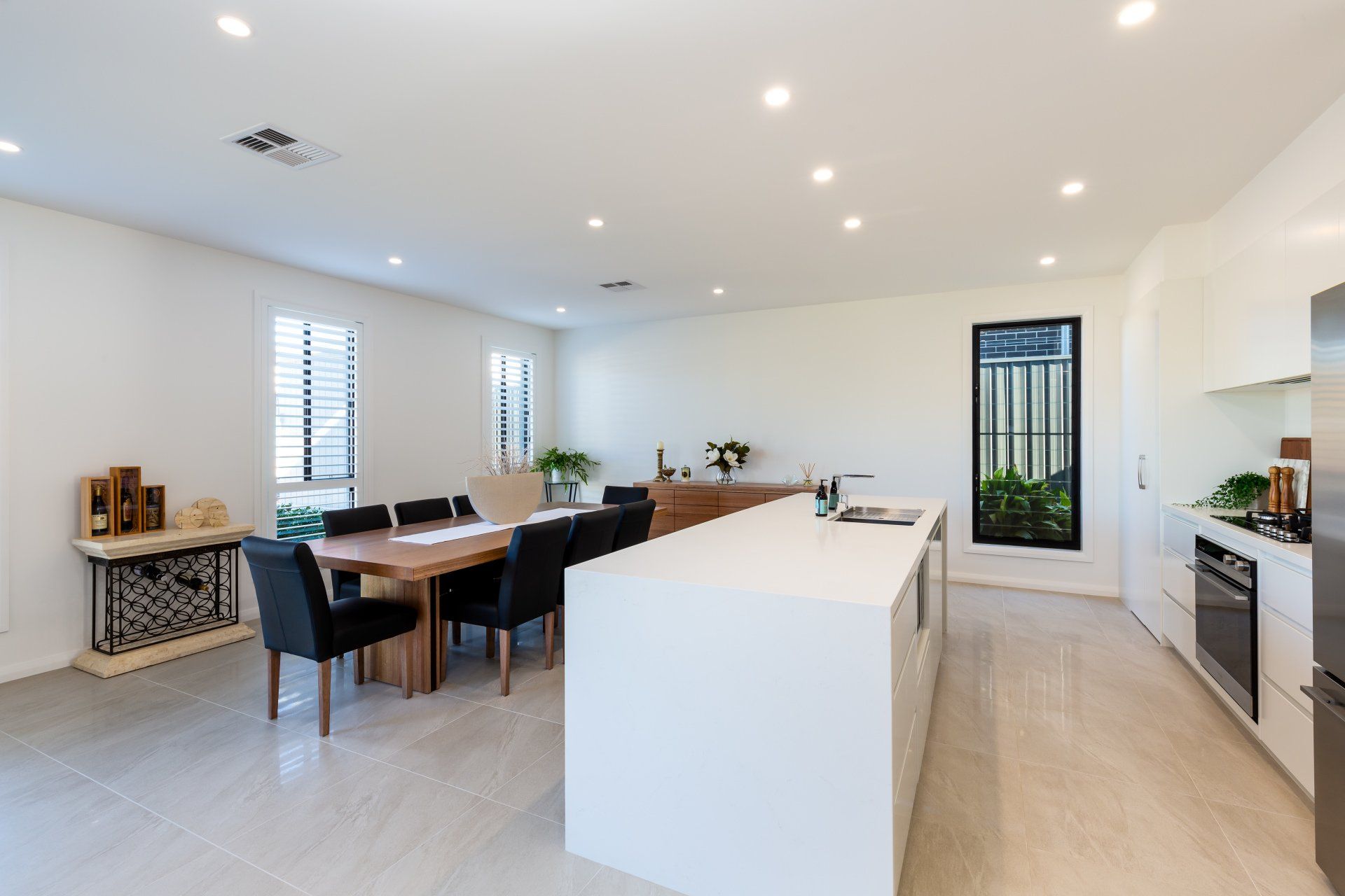Spacious, modern kitchen and dining area with white cabinets, island, dark wood table, and dark chairs.