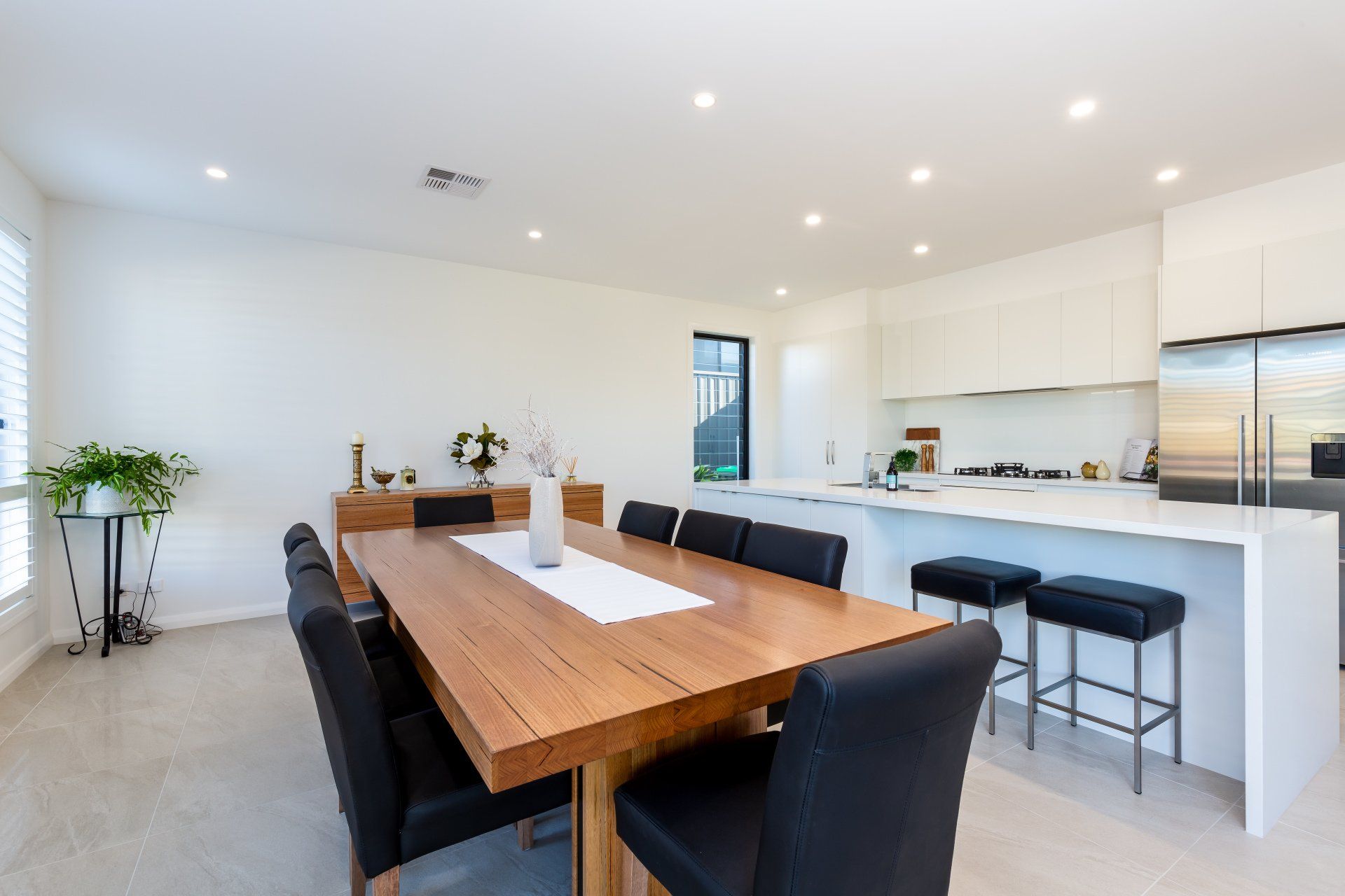 Spacious dining room with a wooden table, black chairs, and a white kitchen with an island.