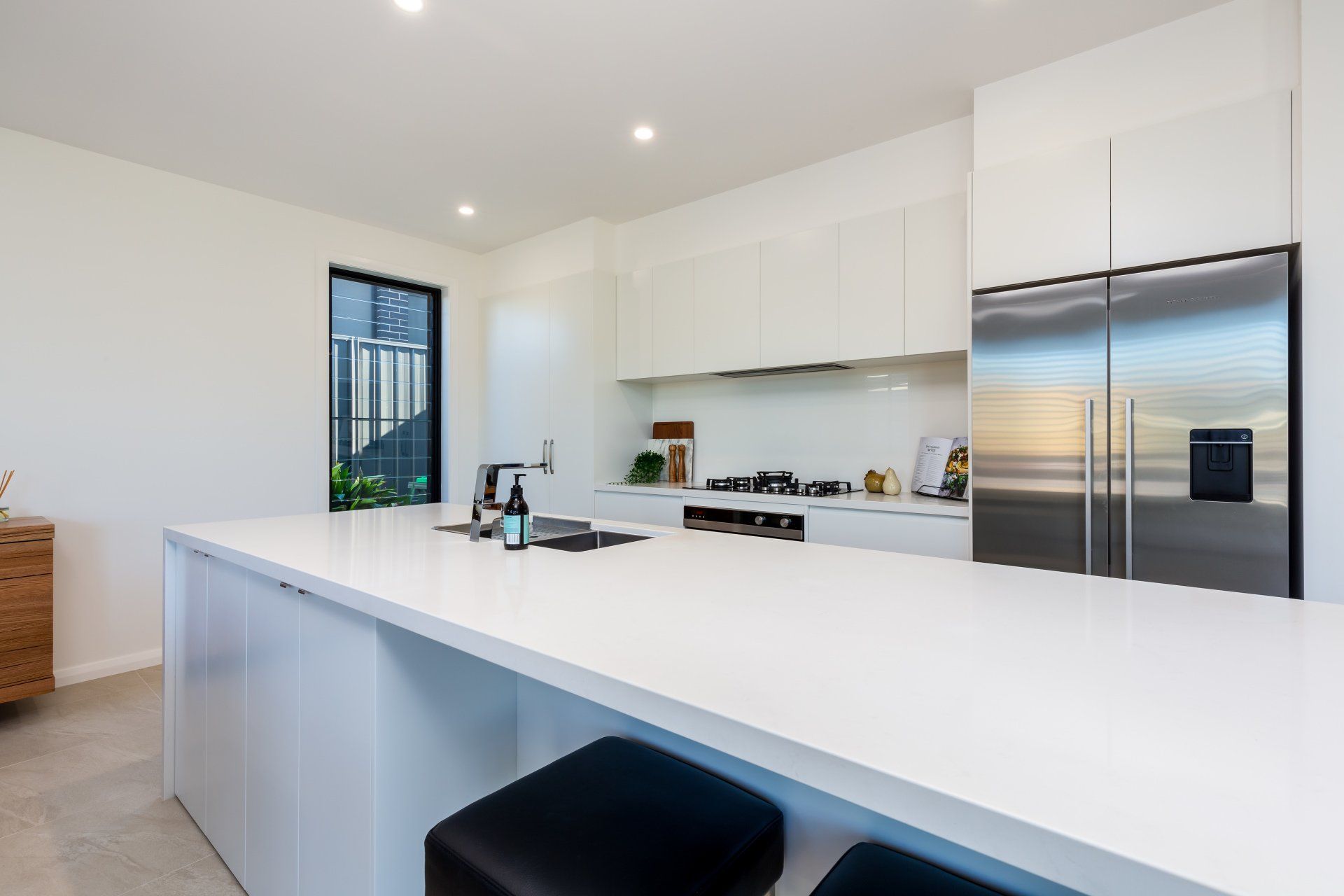 Modern white kitchen with large island and stainless steel refrigerator.