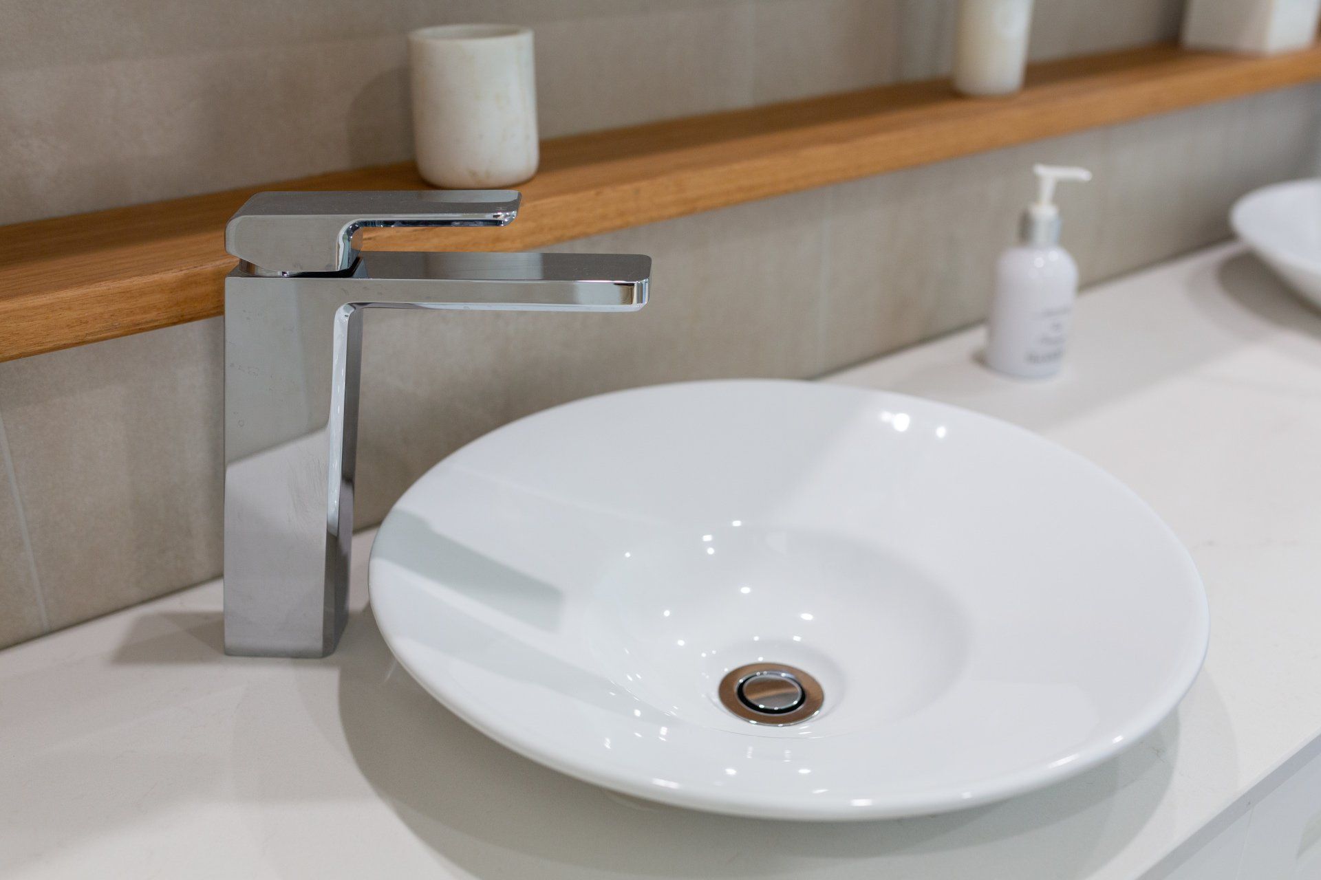 Modern bathroom with a white oval sink, chrome faucet, and wooden shelf with toiletries.