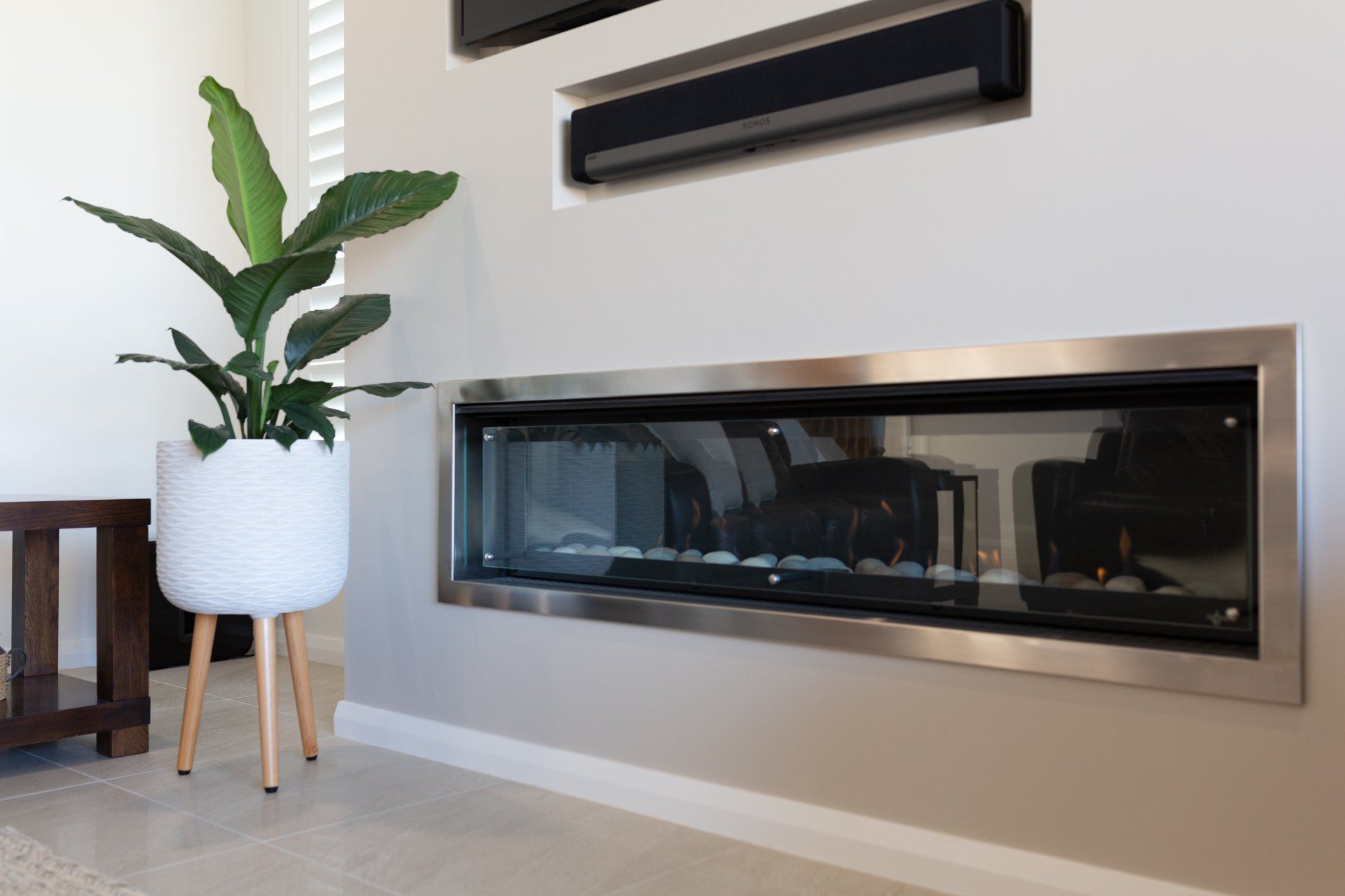 A modern fireplace set in a wall, with a plant in a white pot to its left.