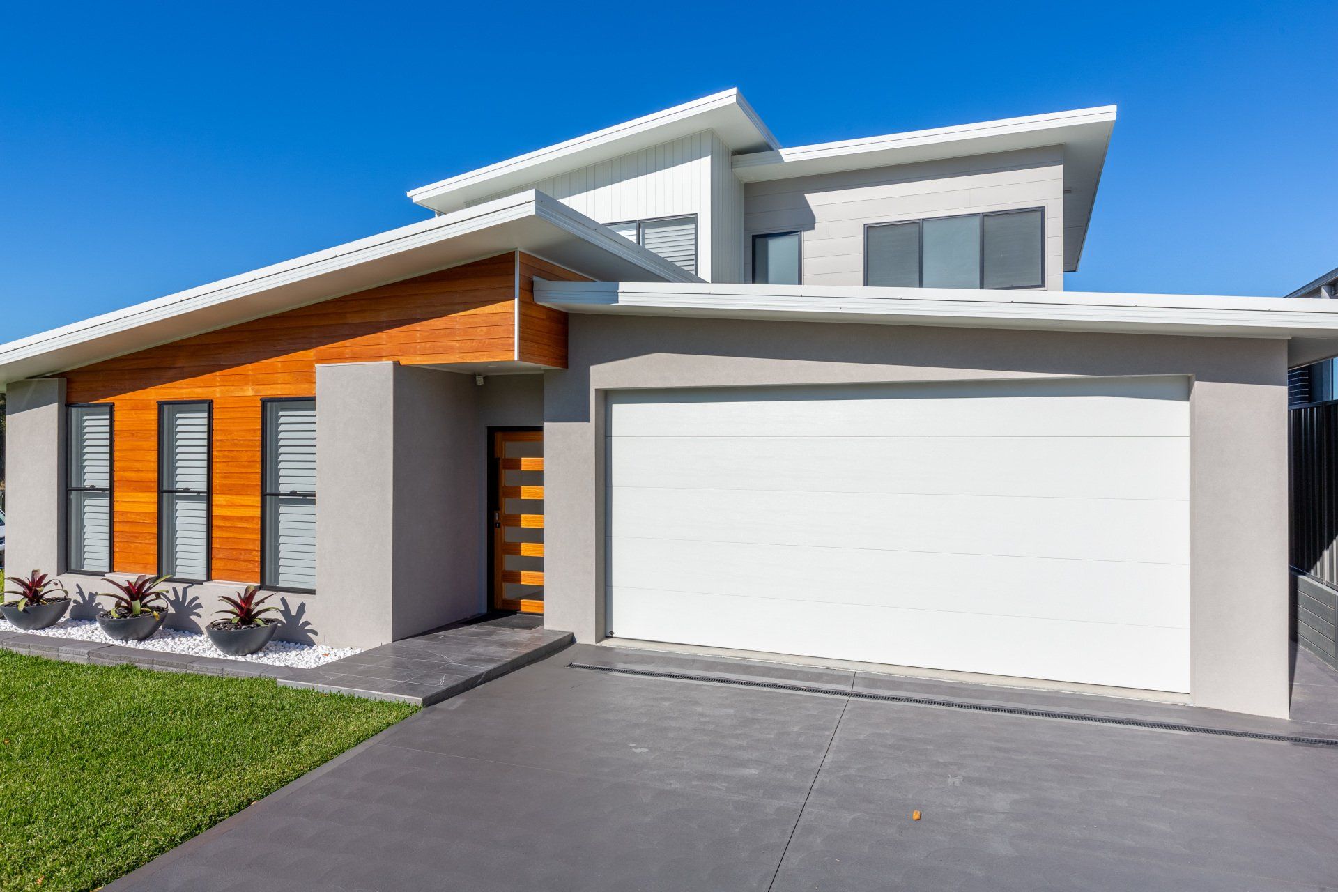 Modern gray and wood-clad house with white garage door on a sunny day.