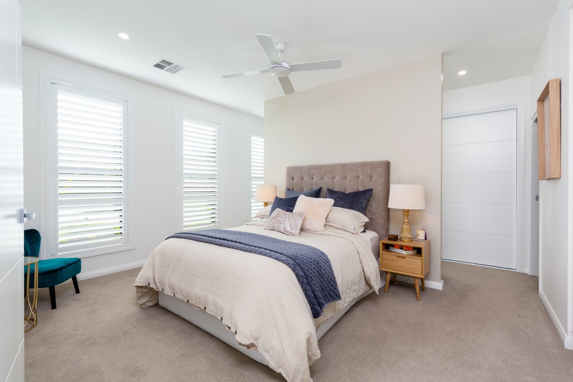 Bedroom with bed, nightstand, blue chair, and window shutters.