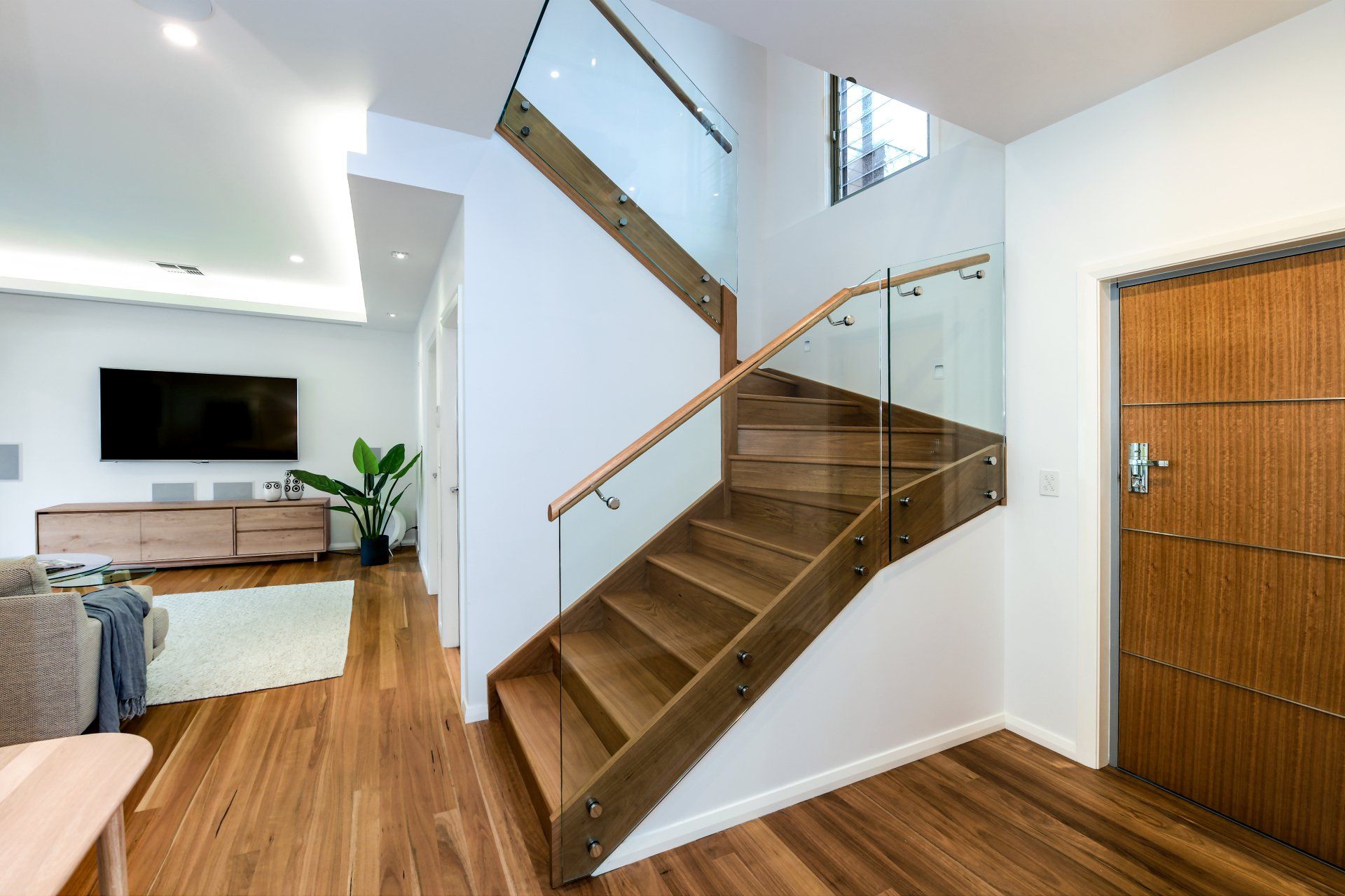 Wooden staircase with glass railing in a modern home.