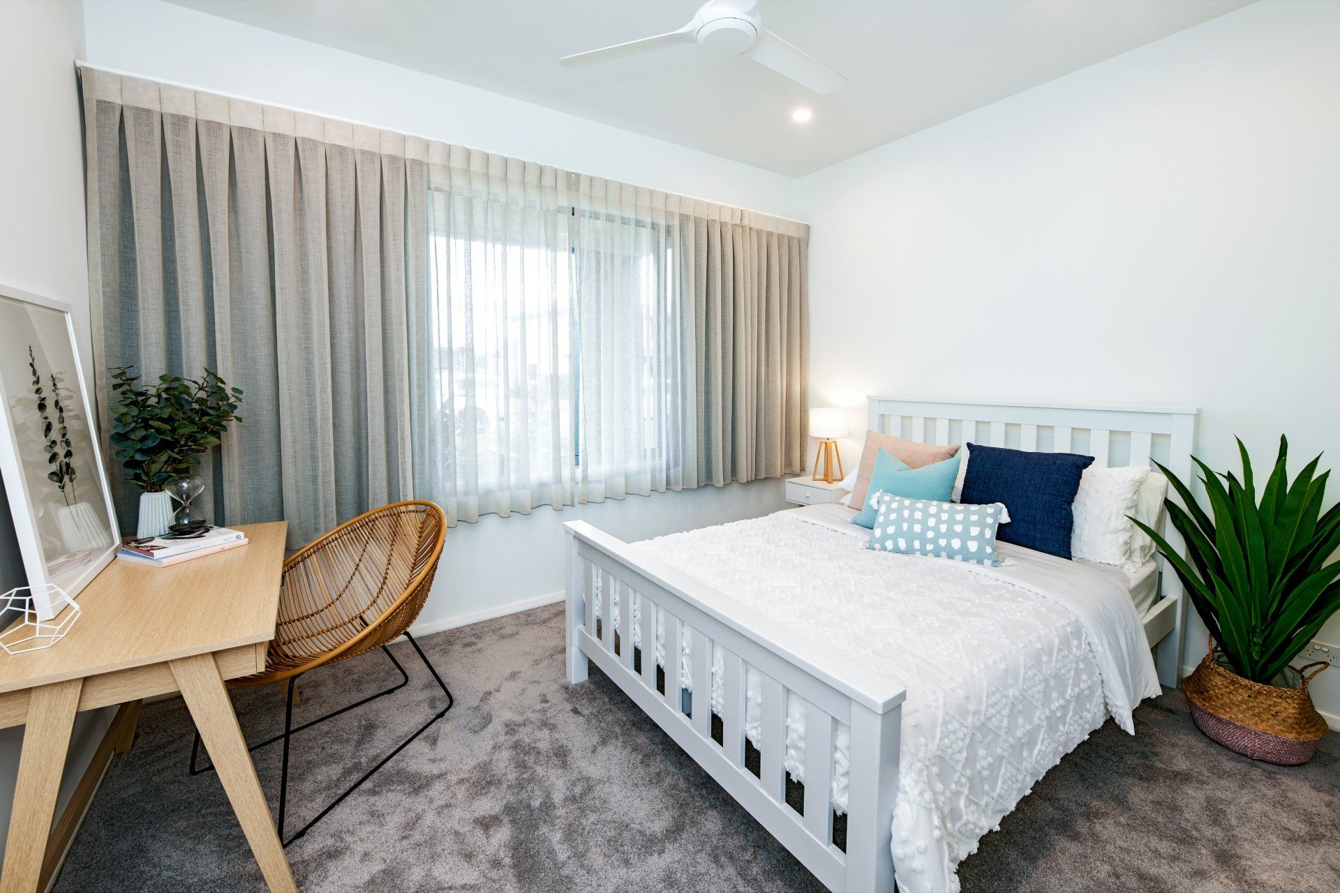 Bedroom with white bed, desk, and large potted plant. Grey curtains, carpet, and walls.