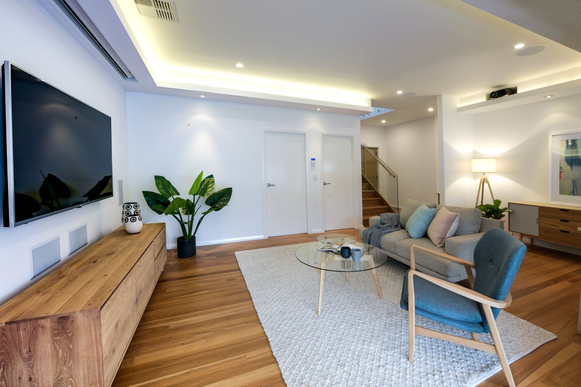 Living room with a large TV, wood furniture, and a gray sofa on a white rug.