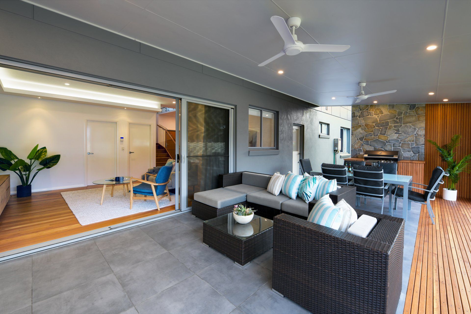 Outdoor living space with gray furniture, dining area, and open sliding glass doors to a living room.