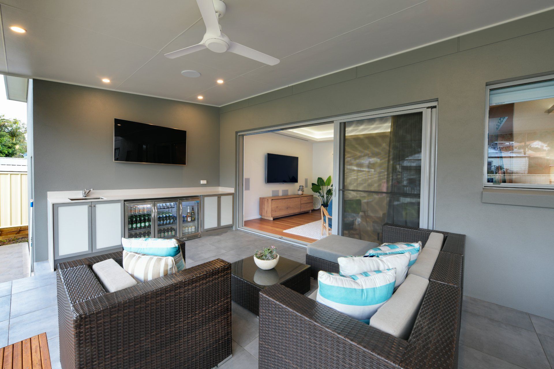Patio with wicker furniture, bar, TV, and sliding glass doors. Grey walls, white ceiling, and a modern setting.