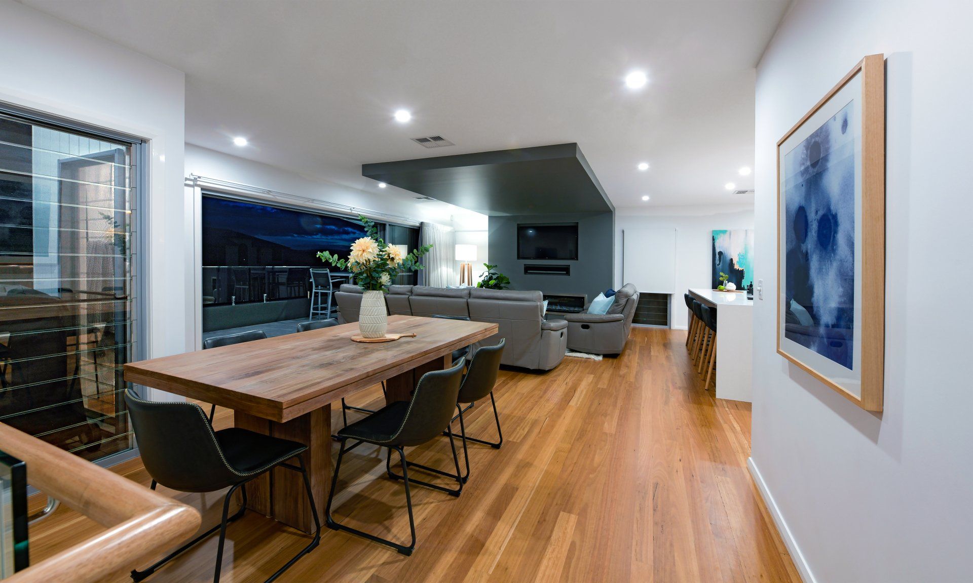 Dining and living area with wood floor, table, and couches. Painting hangs on the wall.