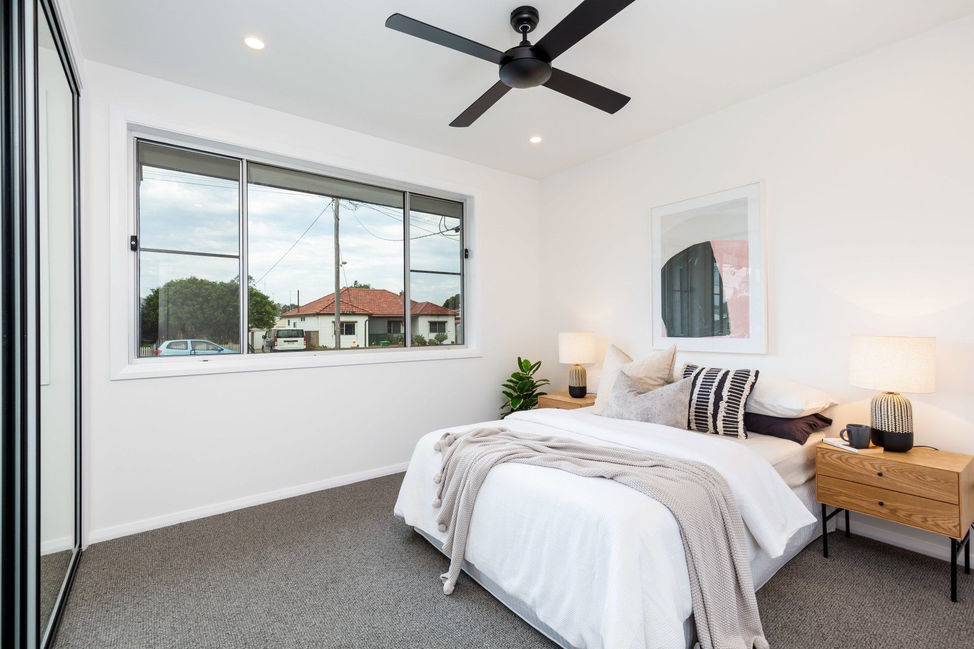 Bedroom with white walls, gray carpet, bed with gray throw, black ceiling fan, and large window.
