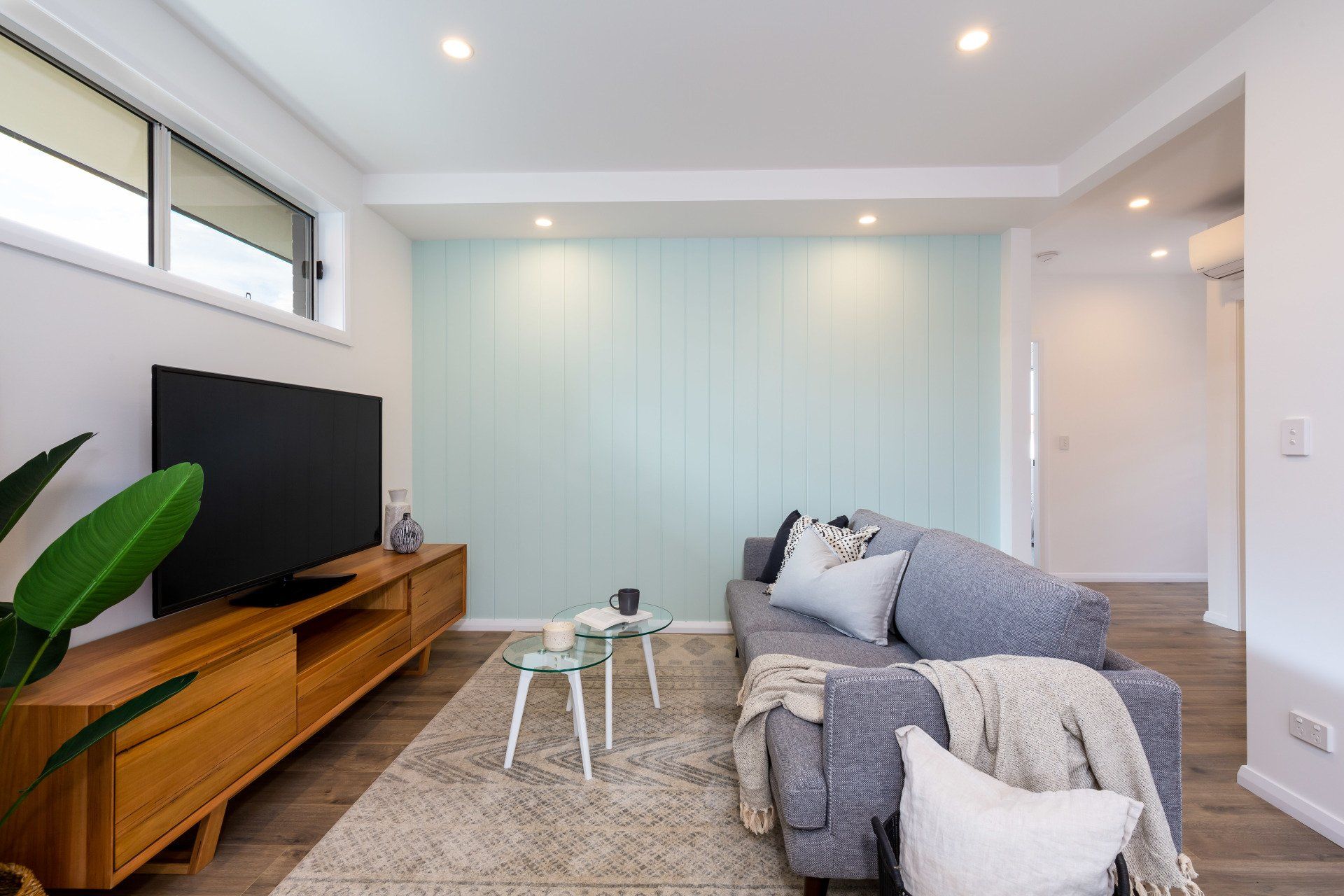 Living room with blue wall, gray sofa, wooden TV stand, and rug.