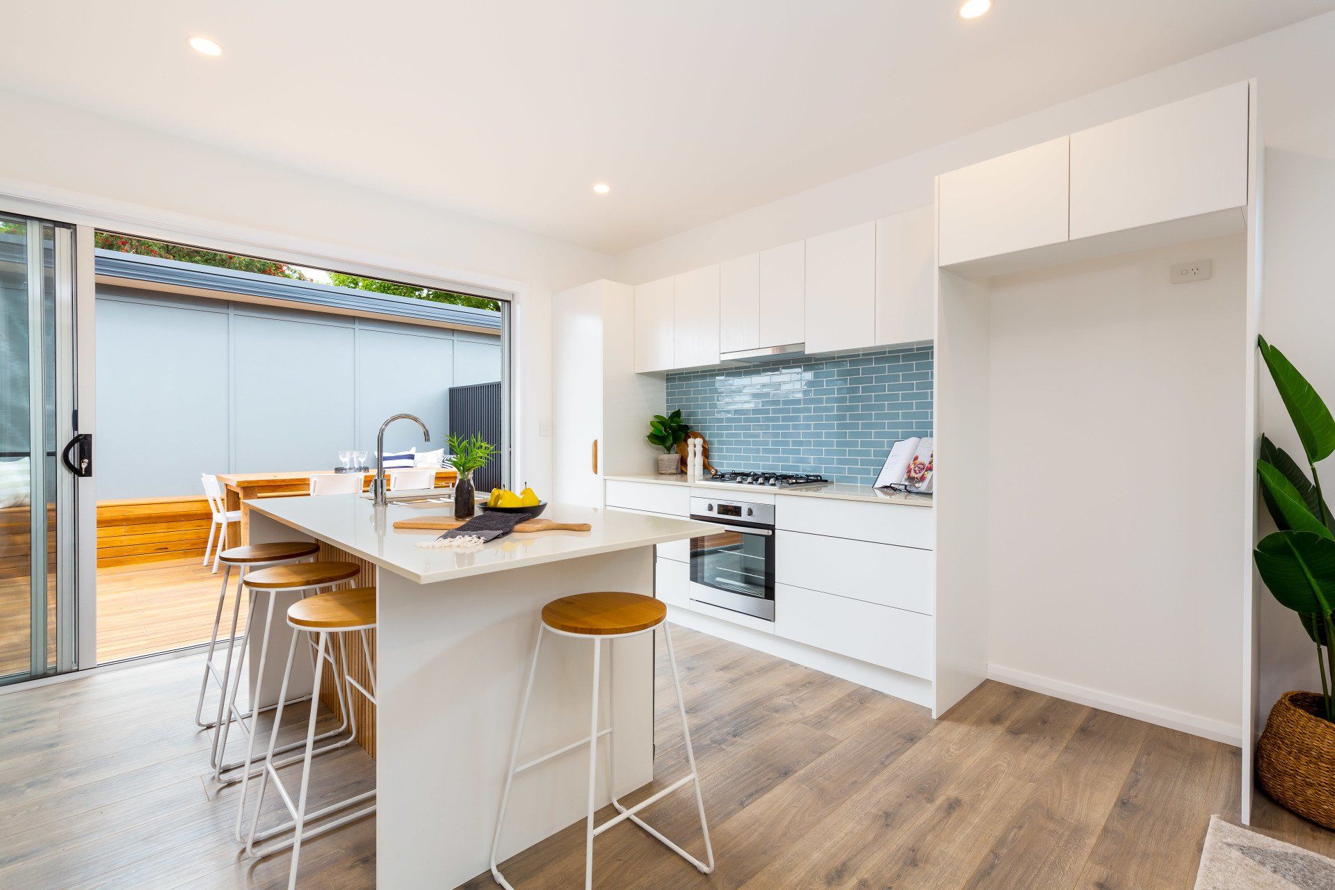 Modern kitchen with white cabinets, island with stools, and open sliding door to patio.