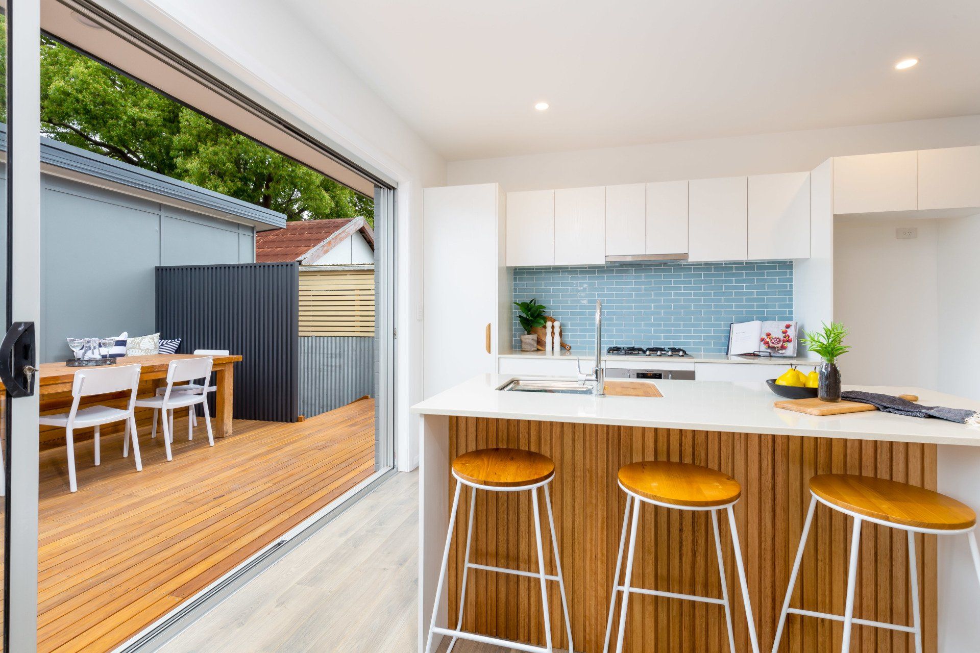 Modern kitchen with a wooden island and stools, opening onto a deck with a dining set.