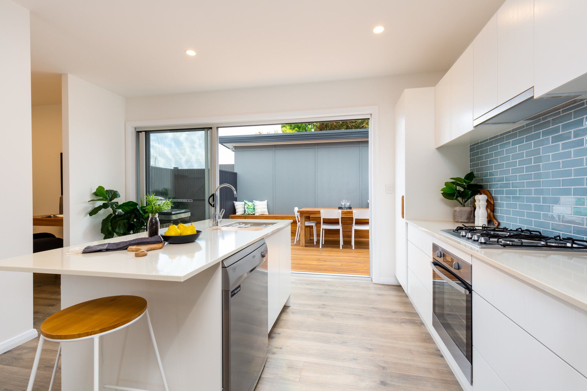 Modern white kitchen with island, open to outdoor dining area.