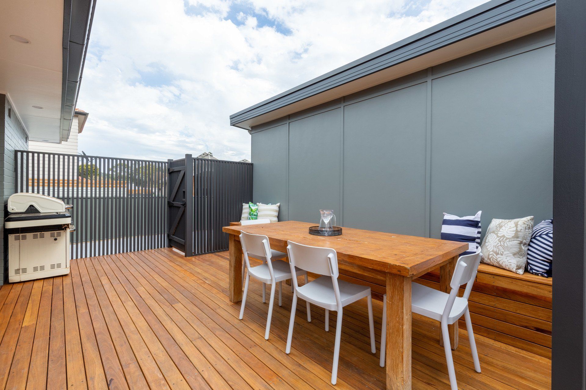 Wooden outdoor patio with table, chairs, grill, and gray wall.