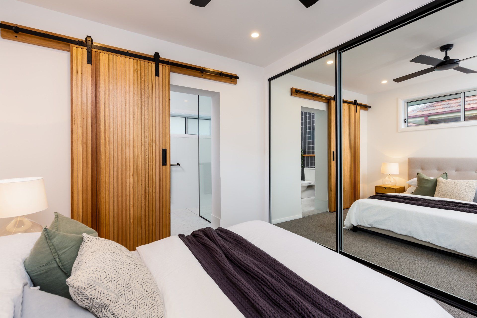 Bedroom with a wooden sliding door to a bathroom and a mirrored closet, showing a bed and a ceiling fan.