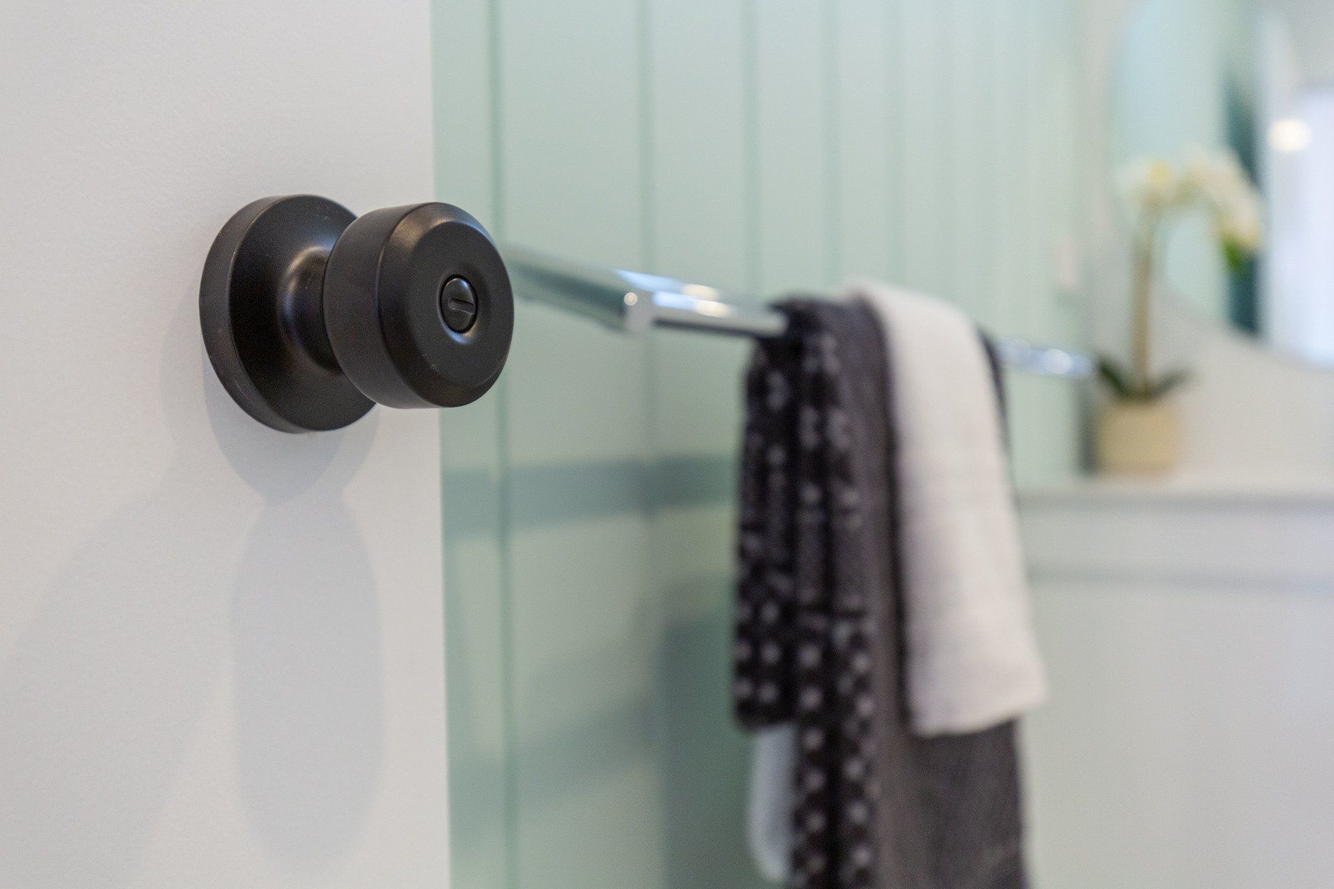 Black doorknob on white door, in a bathroom with a towel rack.