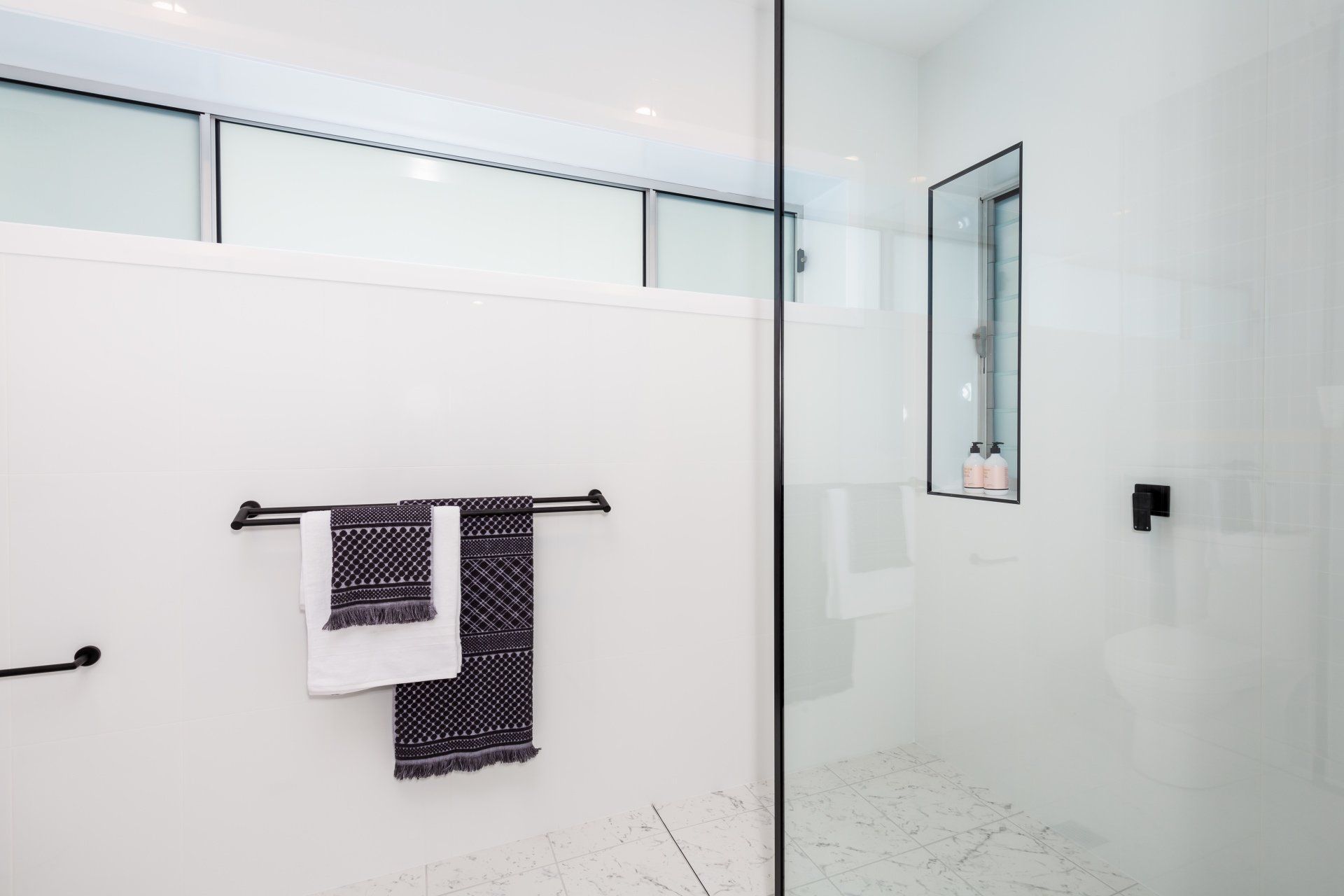 Modern white bathroom with glass shower, black towel rack, and towels.