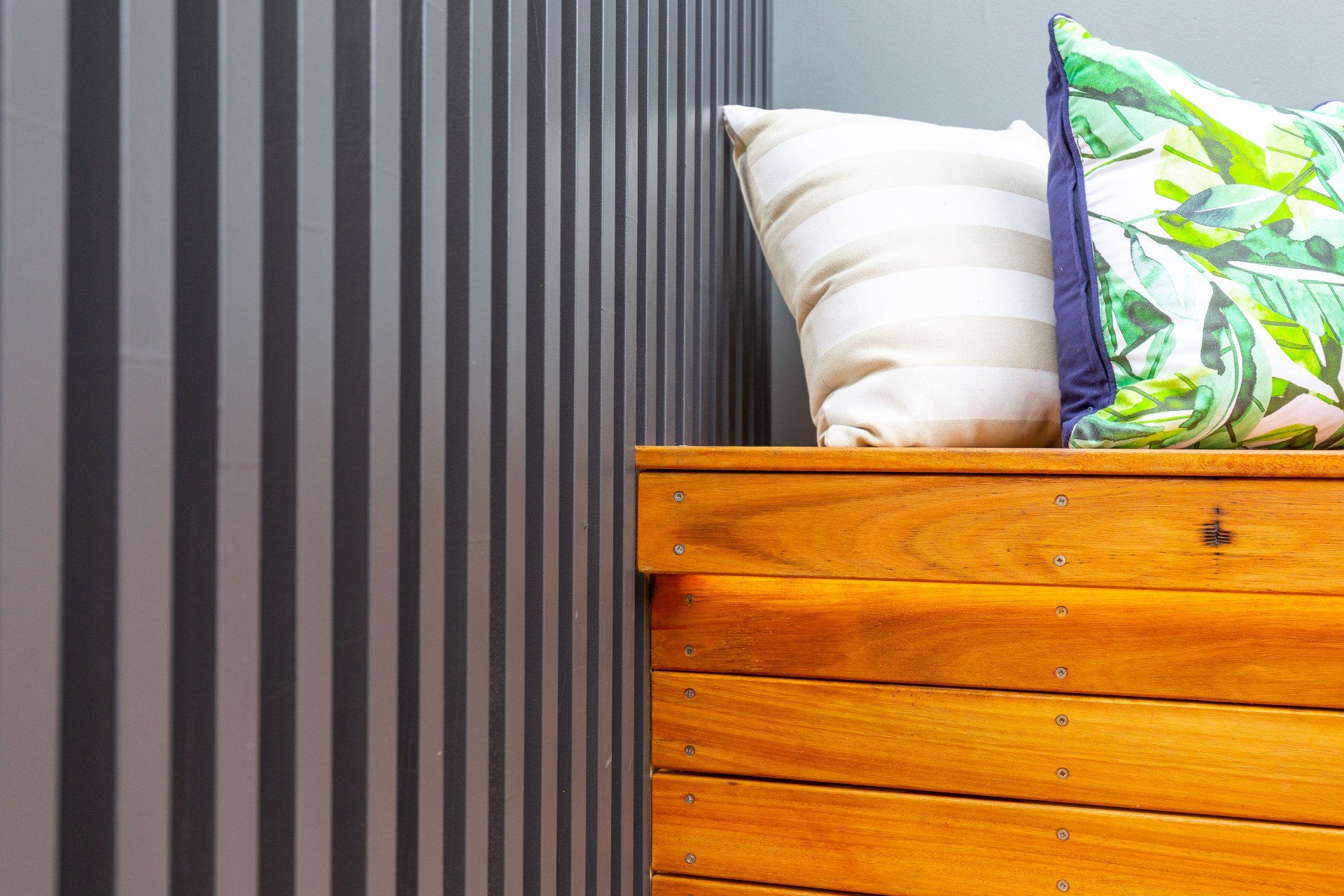 Striped wall corner with wooden chest and patterned pillows.