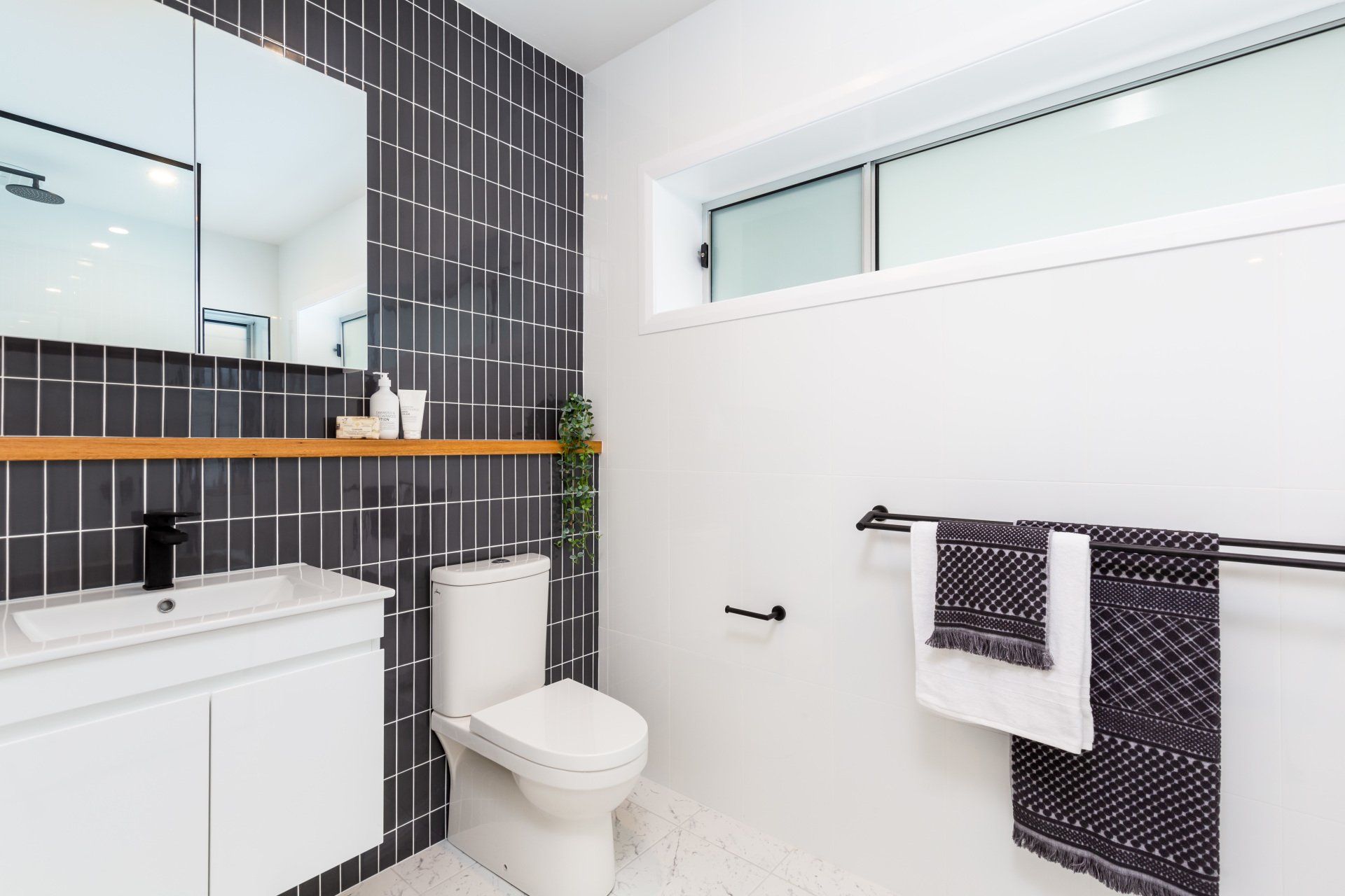 Modern bathroom with dark tile accent wall, white fixtures, and a window.