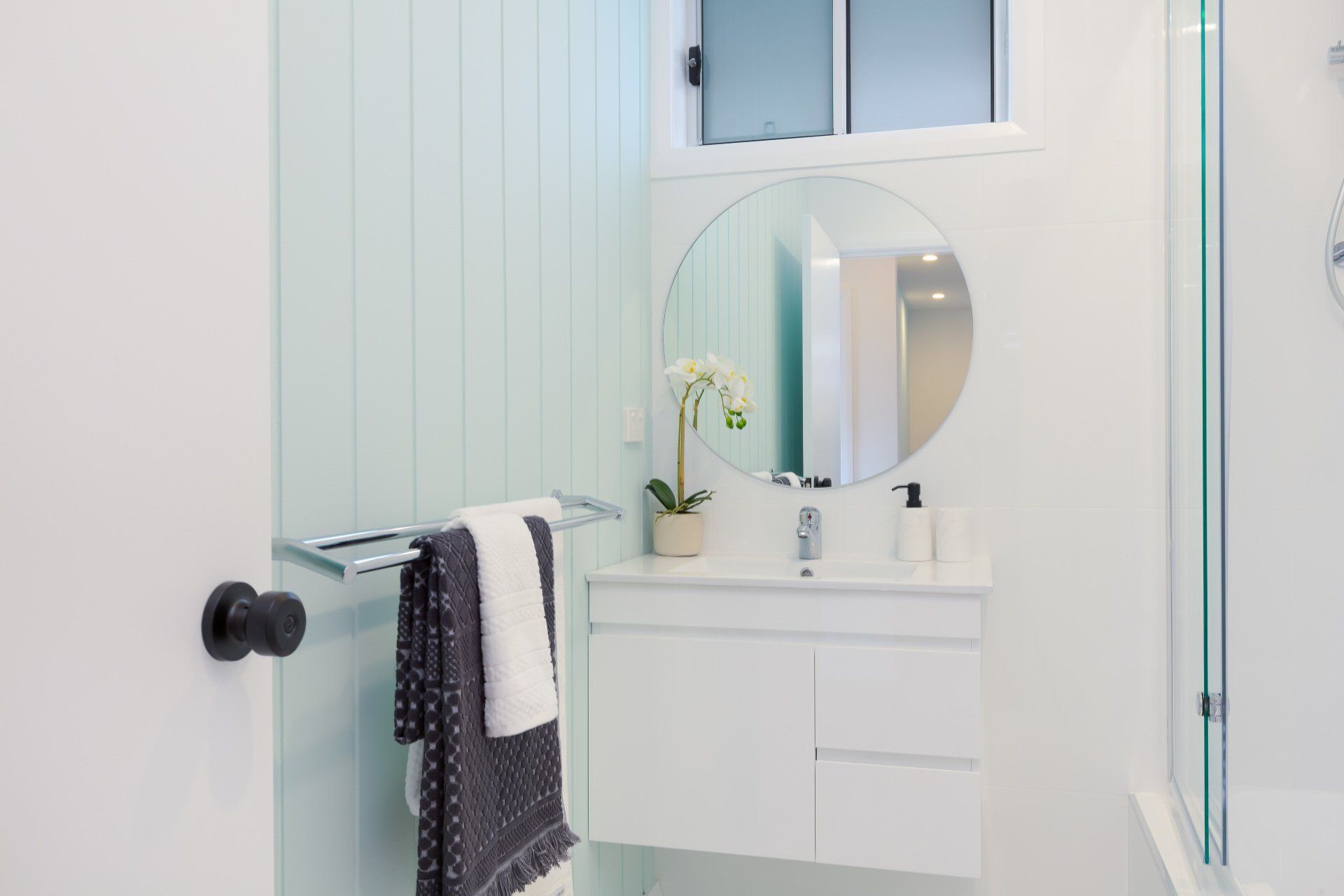 Bathroom with white vanity, round mirror, and mint green paneling.