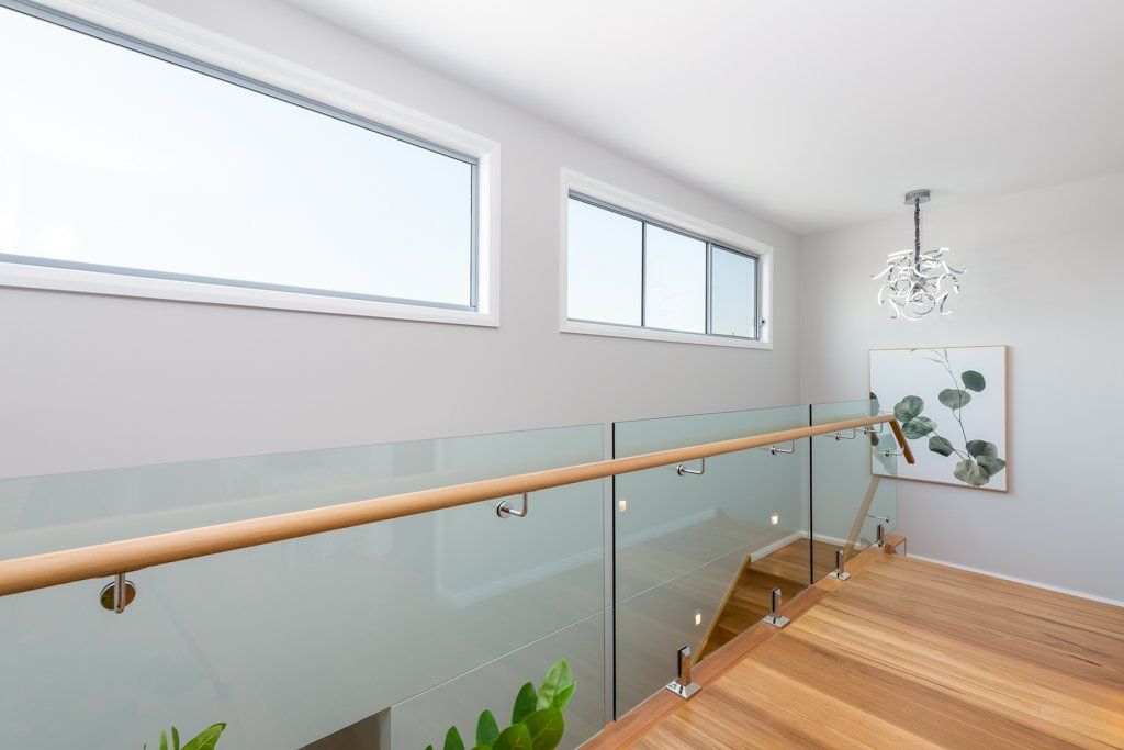 Interior view of a staircase with glass railing, wooden steps, and two windows.