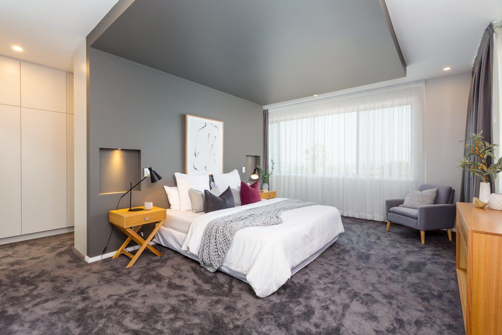 Modern gray bedroom with a bed, armchair, and wooden furniture.