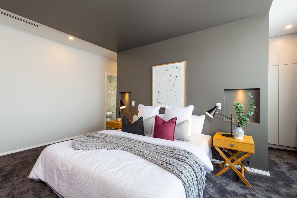 Modern bedroom with gray walls, bed, colorful pillows, and a wooden bedside table.