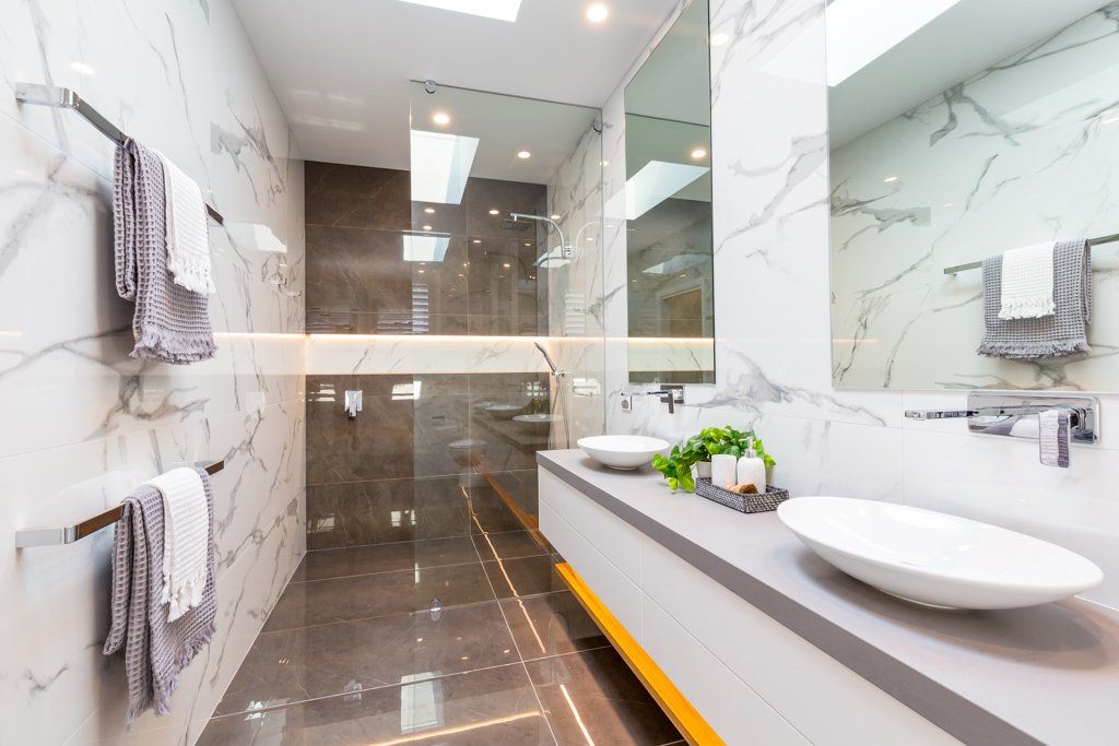 Modern bathroom with marble walls, a long vanity with two sinks, and a glass shower.