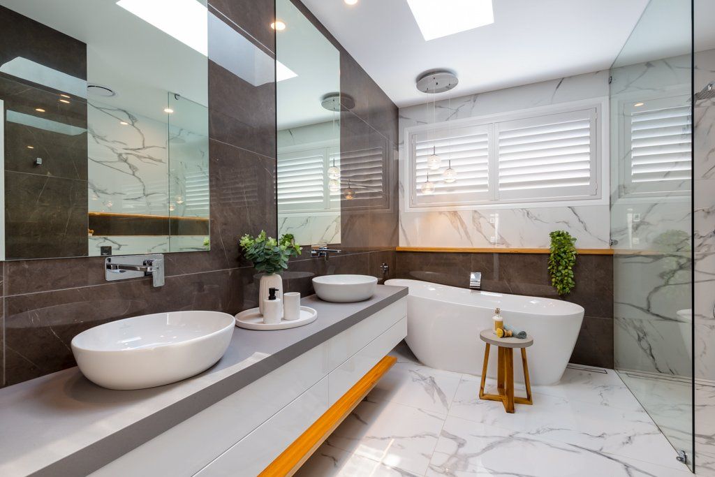 Modern bathroom with marble, dual sinks, bathtub, and skylight.