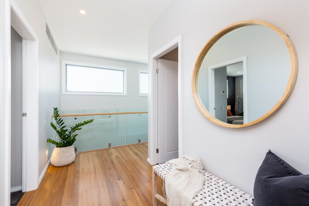 Hallway with wooden floor, round mirror, bench with blanket, and plant in a woven pot.