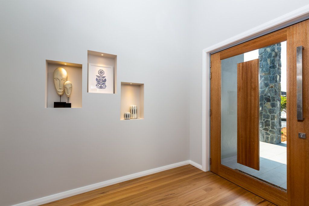Entryway with wooden door, recessed wall niches displaying art, and wood flooring.