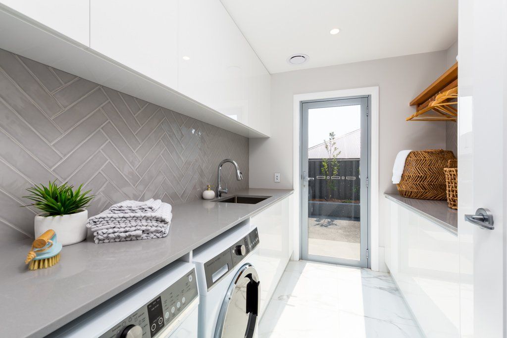 Modern laundry room with gray countertops, washing machine, and a door to the outside.