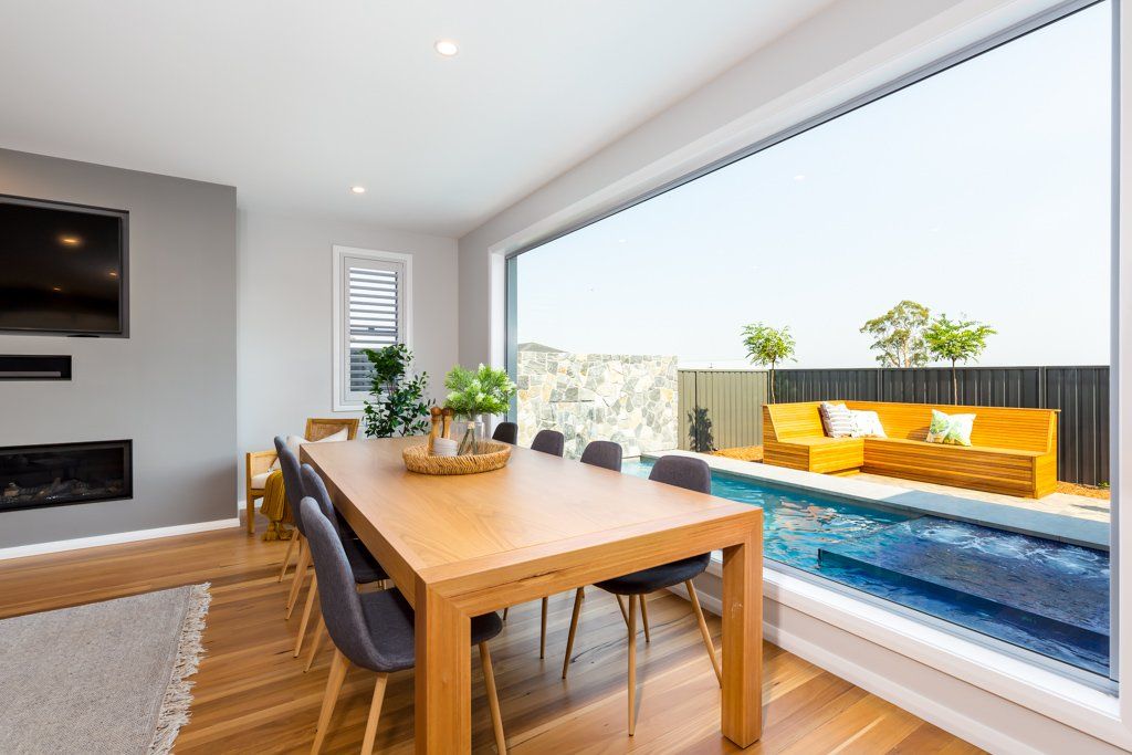 Dining room with large wooden table, grey chairs, overlooking a pool and outdoor seating.