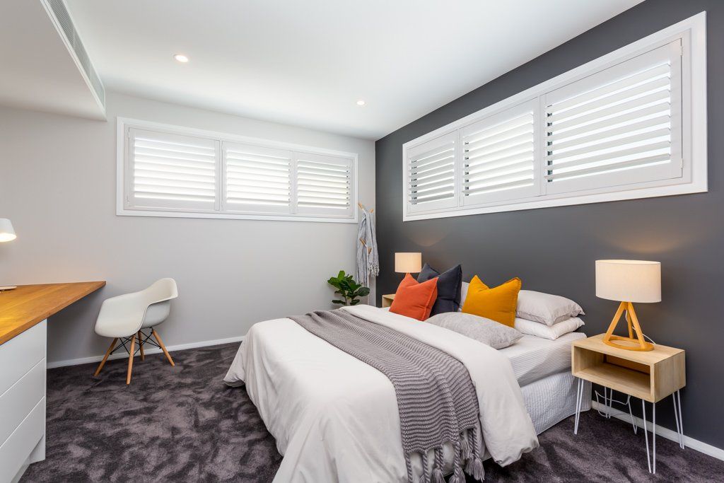 Bedroom with dark grey accent wall, bed with colorful pillows, white shutters, desk and chair.