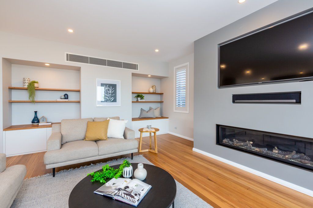 Modern living room with sofa, built-in shelves, fireplace, TV, and hardwood floors.