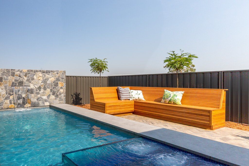 Poolside seating area with wooden benches, throw pillows, and a pool.