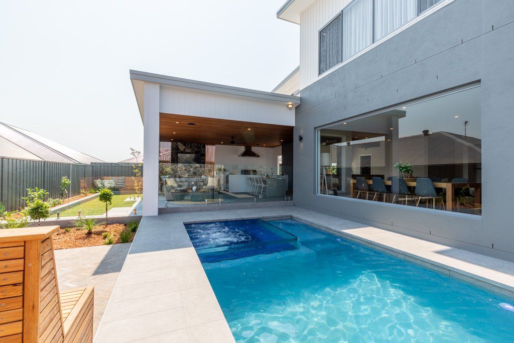 Backyard pool with house, outdoor kitchen and seating area, bright blue water.