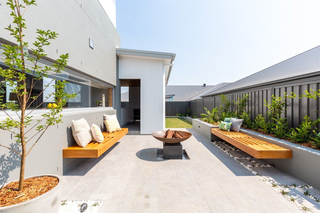 Modern backyard with wooden benches, fire pit, and greenery.