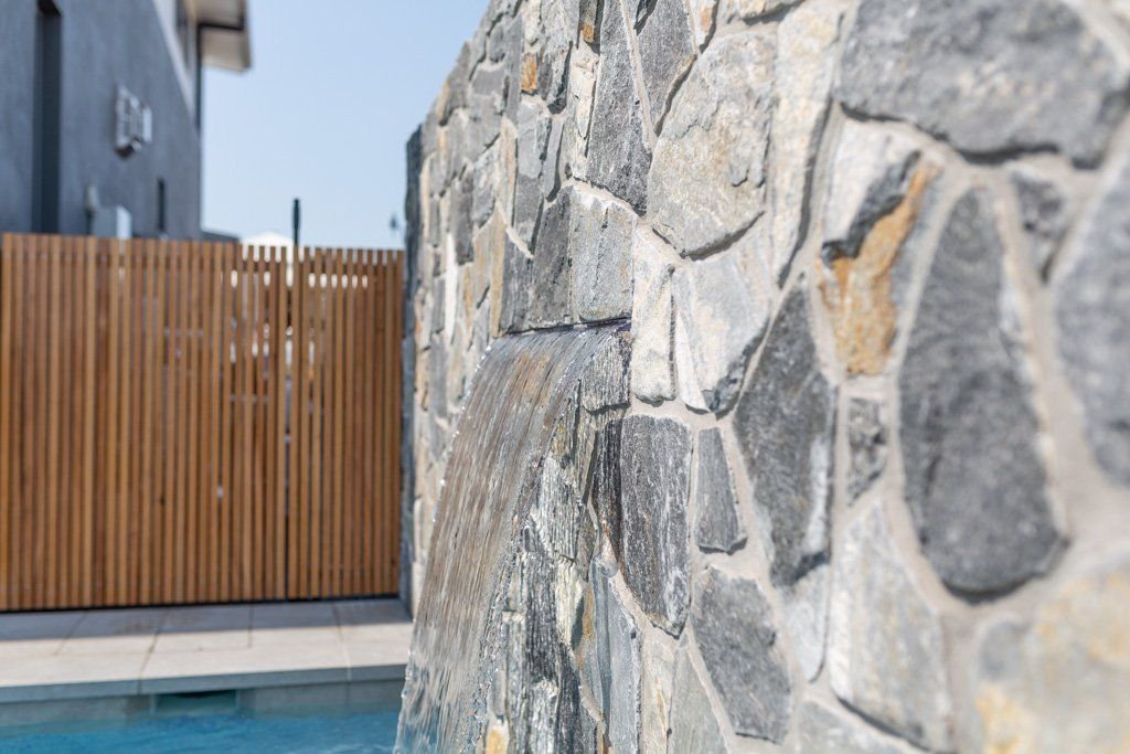 Stone wall next to a pool with wooden fence in the background.