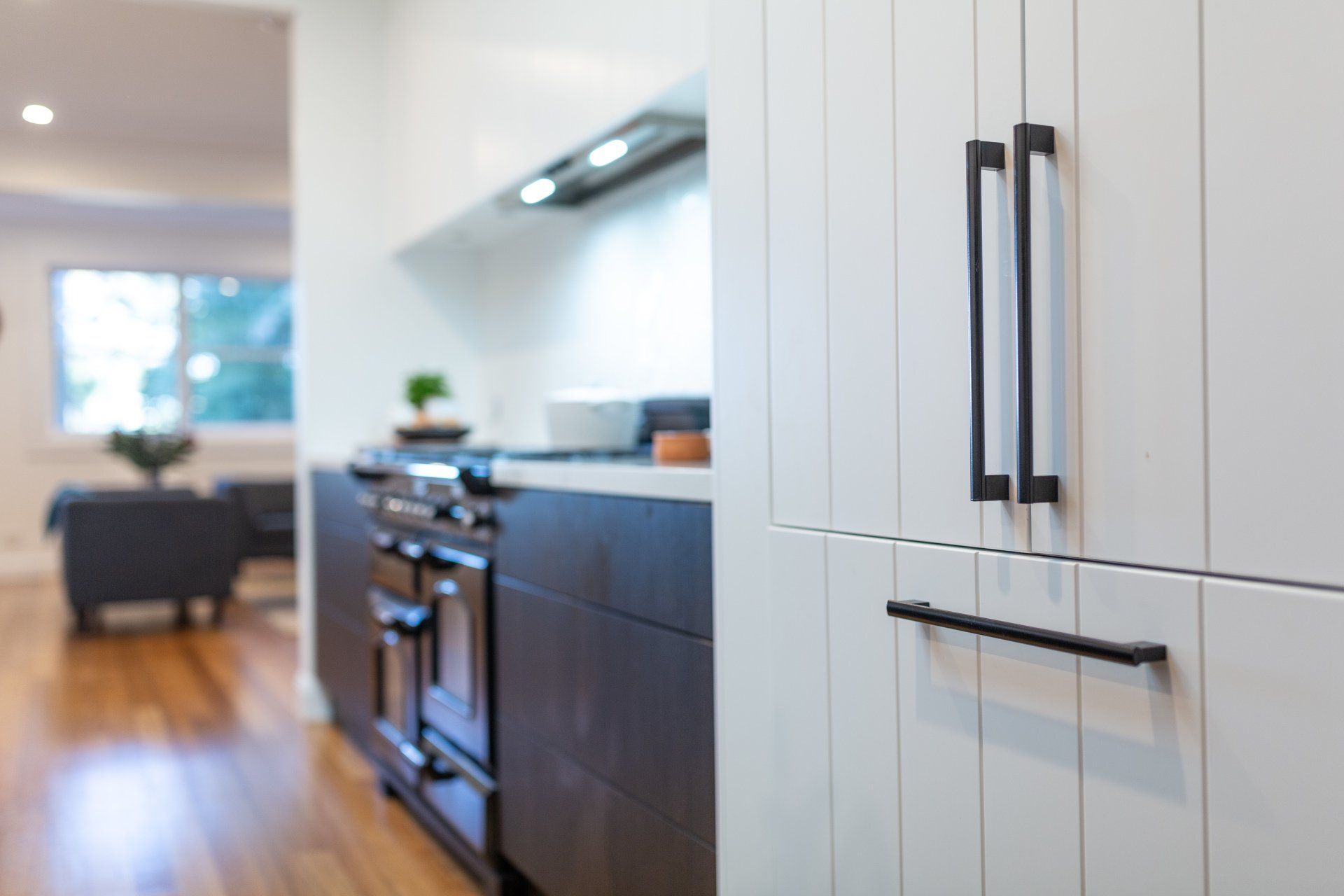 White kitchen cabinet with black handles; stovetop, and view of living area with wooden floors.