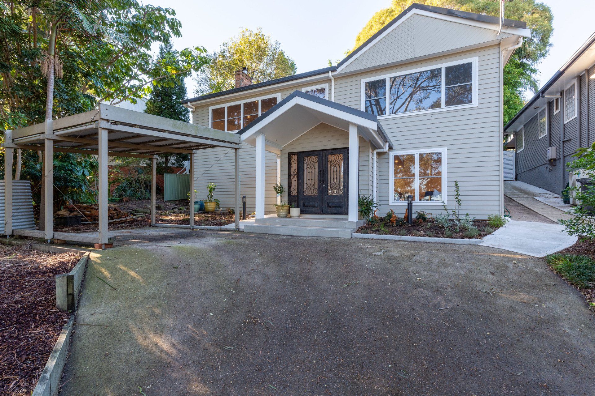 Two-story house with a carport. Light gray siding, dark double front doors, and a driveway.