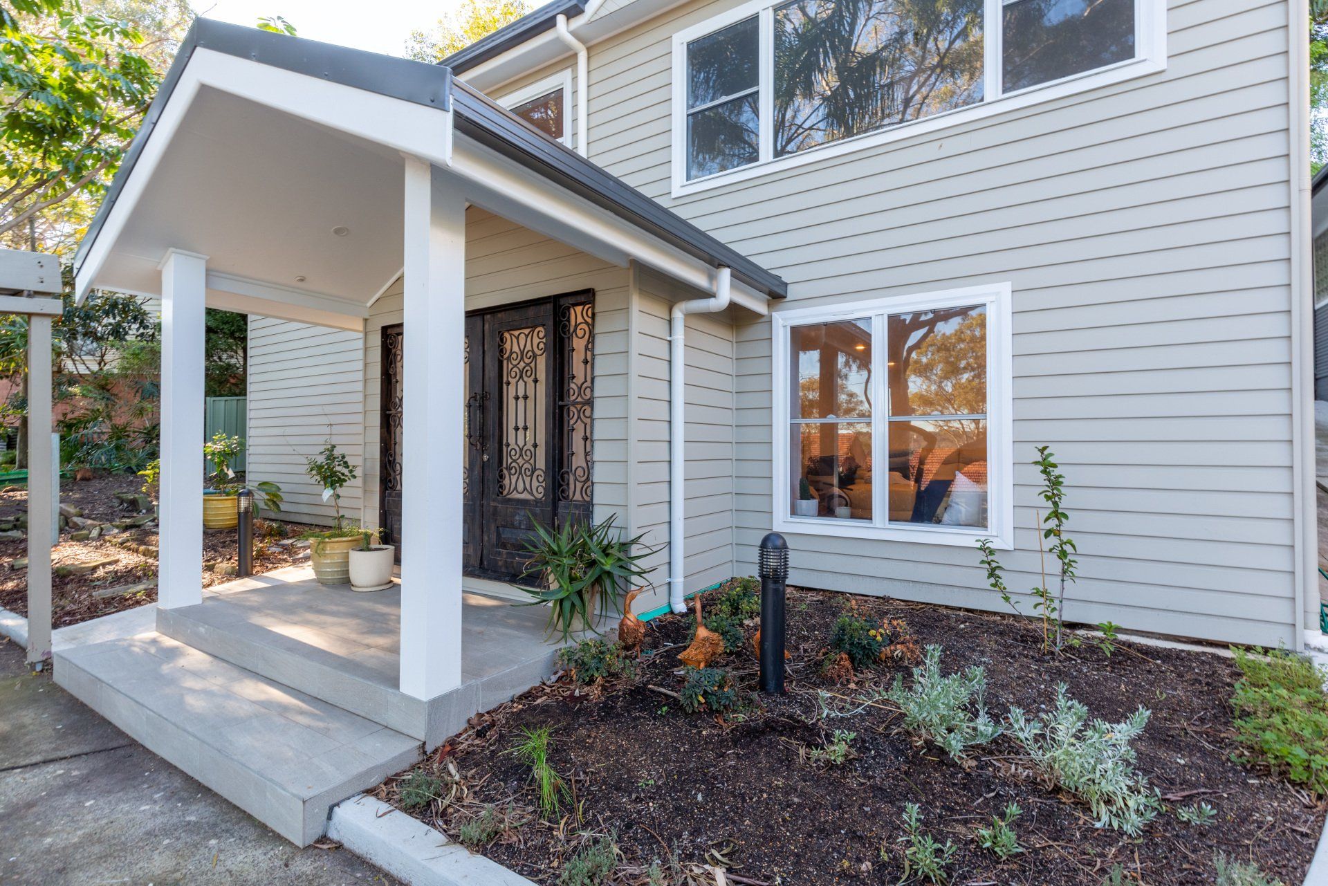 Gray house with porch, steps, and a black door, surrounded by a garden bed.