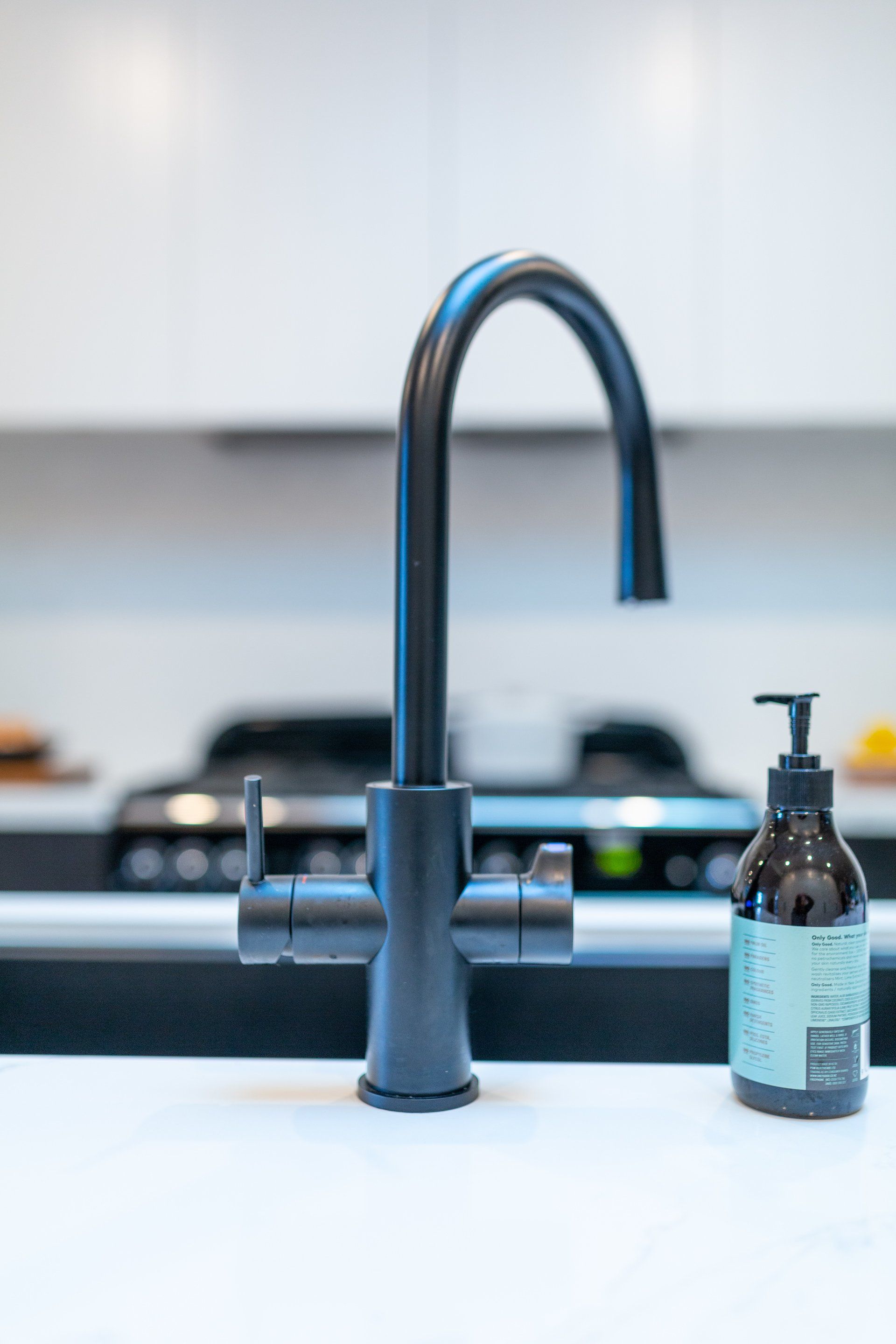 Black kitchen faucet with soap dispenser on a white countertop.