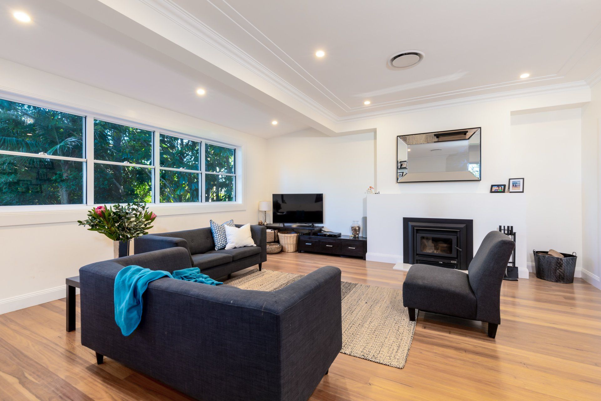 Living room with dark blue couches, fireplace, TV, and large windows overlooking trees.