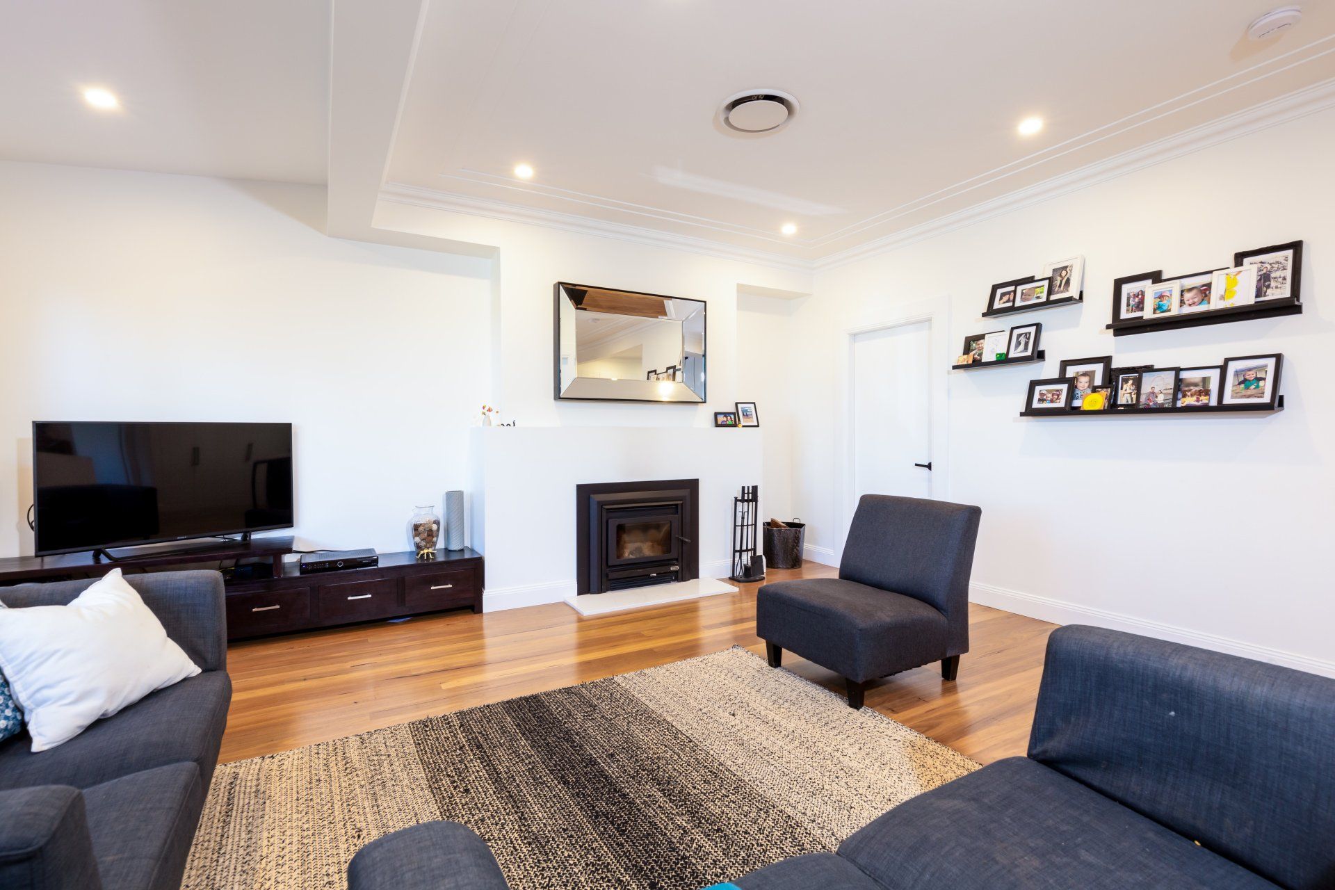 Living room with fireplace, TV, dark gray furniture, hardwood floors, and a rug.